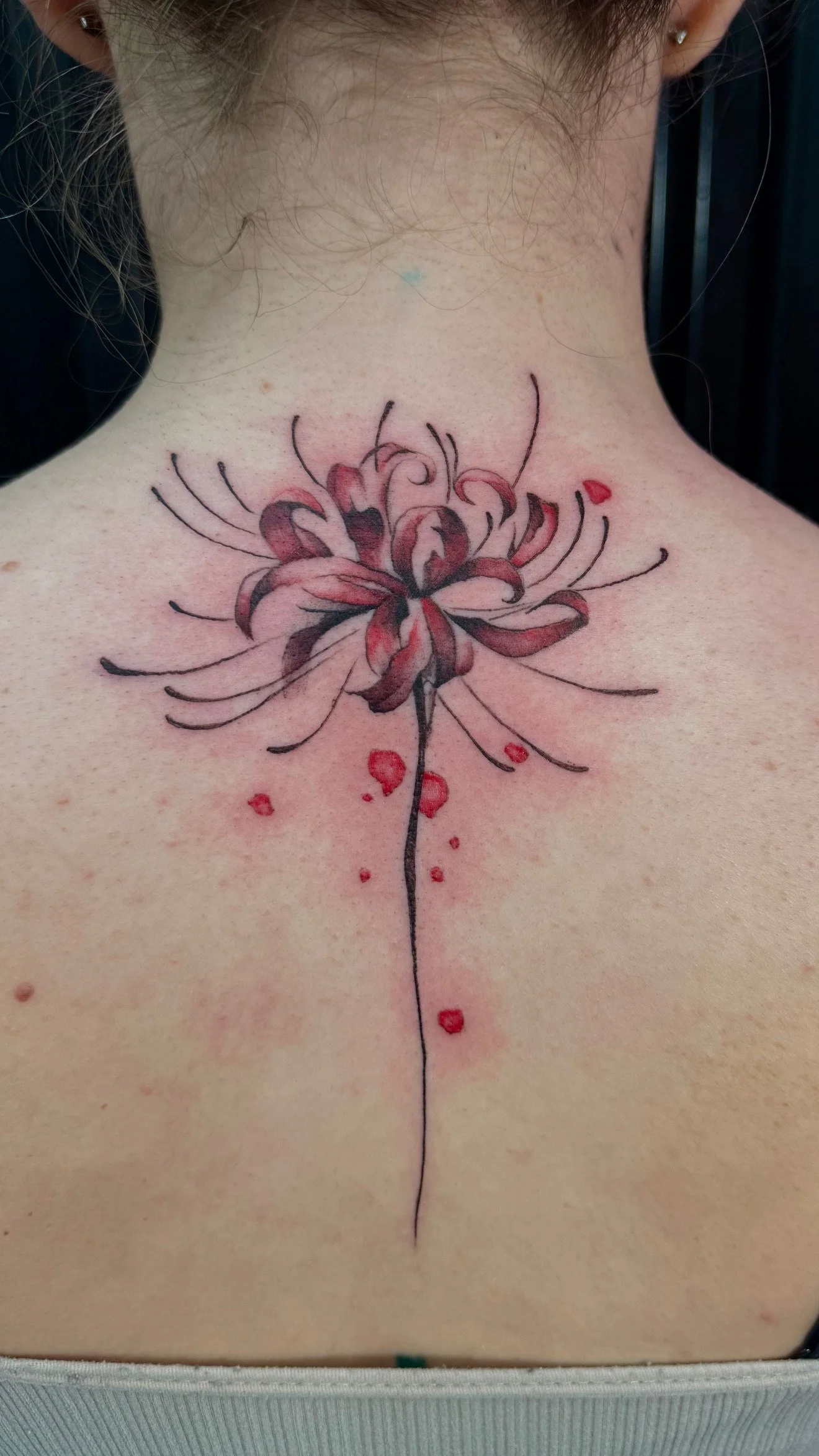 Tattoo of a blooming flower with dark pink and black petals on the upper back.