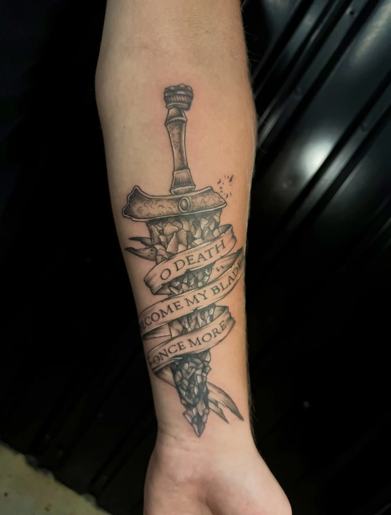 Tattoo of a shattered sword with a banner wrapped around it reading "O Death" and "Once My Blade Become More."