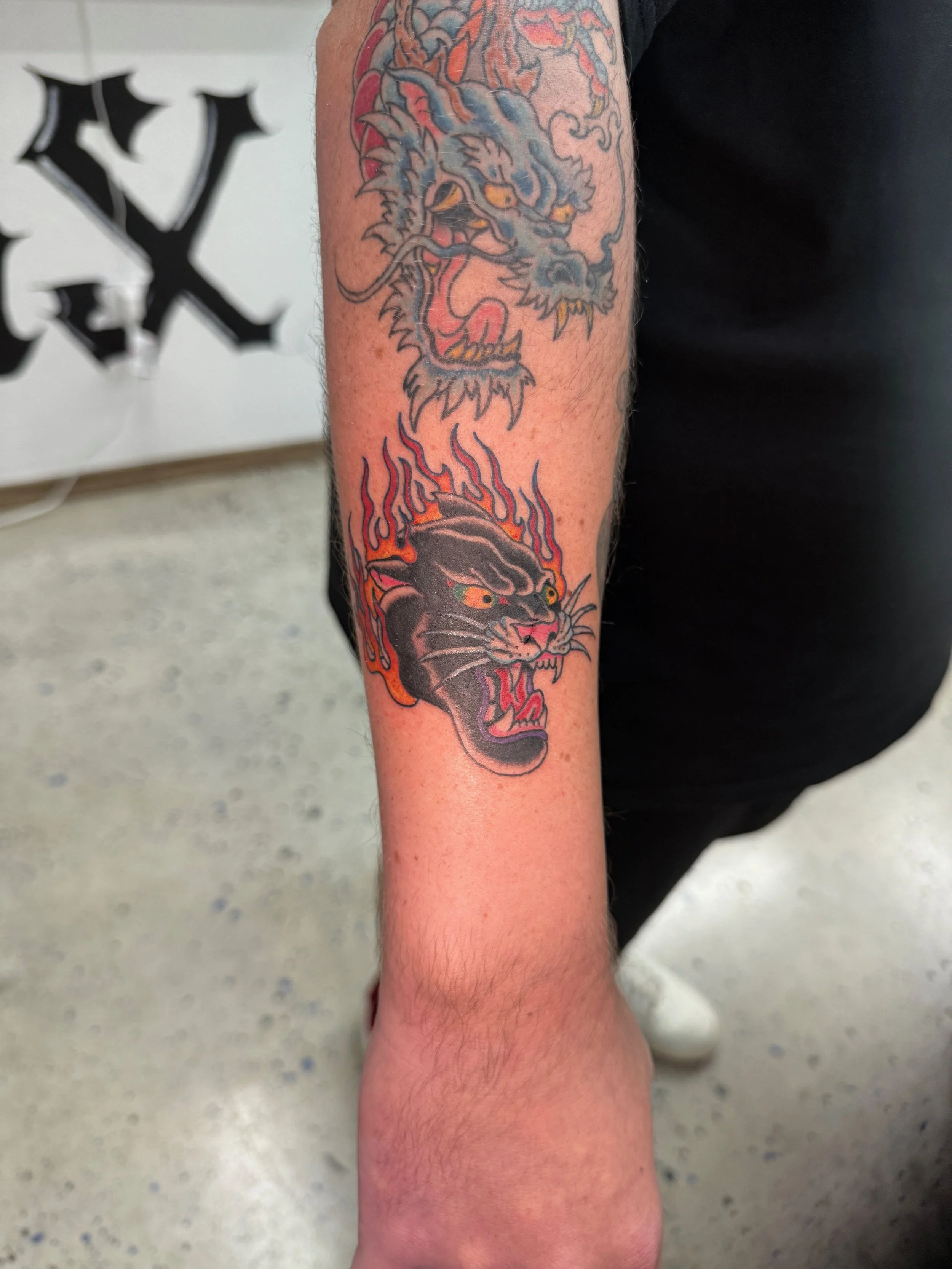 Tattoo of a black panther with flames on its head and upper body on a person's arm, with a traditional style dragon above it.