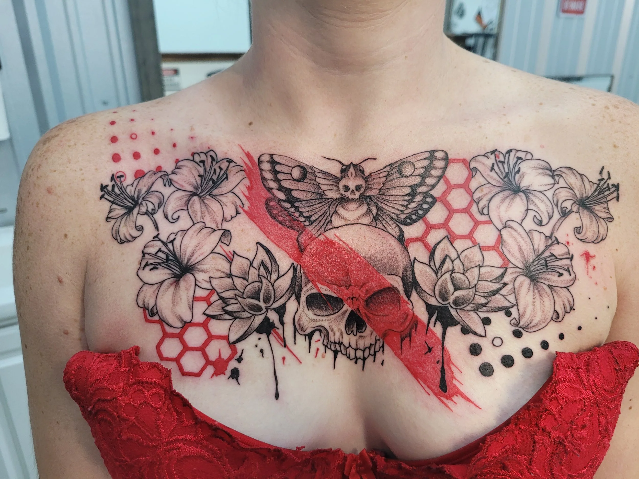 A chest tattoo featuring a large skull with a red lightning bolt, surrounded by flowers, honeycomb patterns, and a moth with a skull face