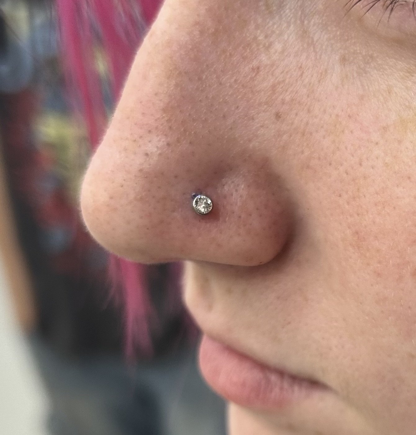 Close-up of a person's nose with a small, clear gemstone nose stud piercing.