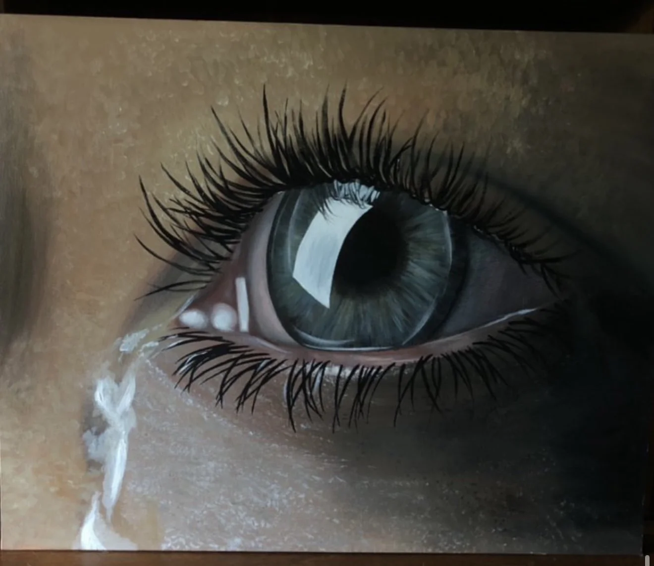 Close-up of a human eye with long eyelashes and tears streaming down the cheek.