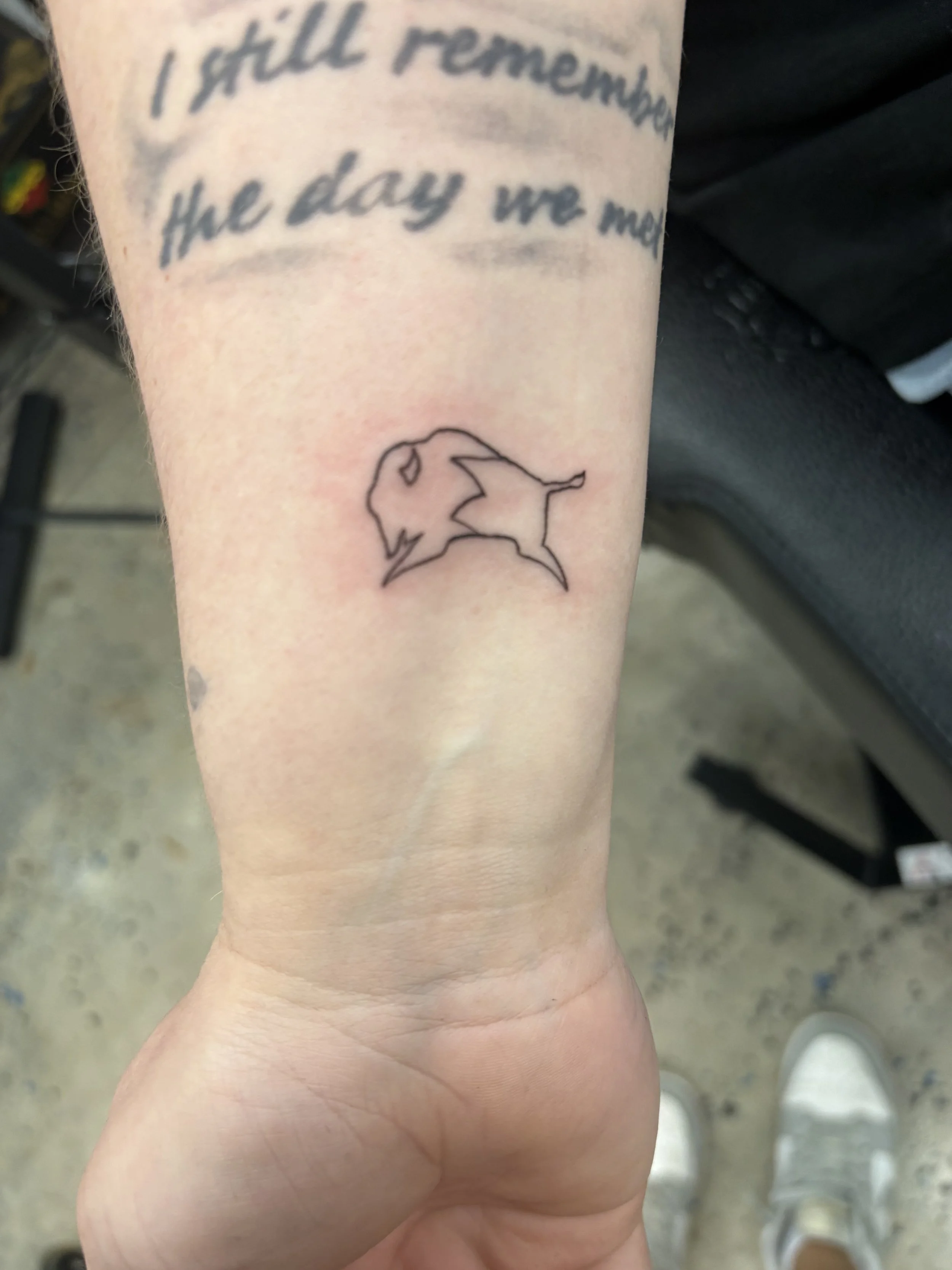 Tattoo on person's arm that says 'I still remember the day we met' with a line art outline of a lion.