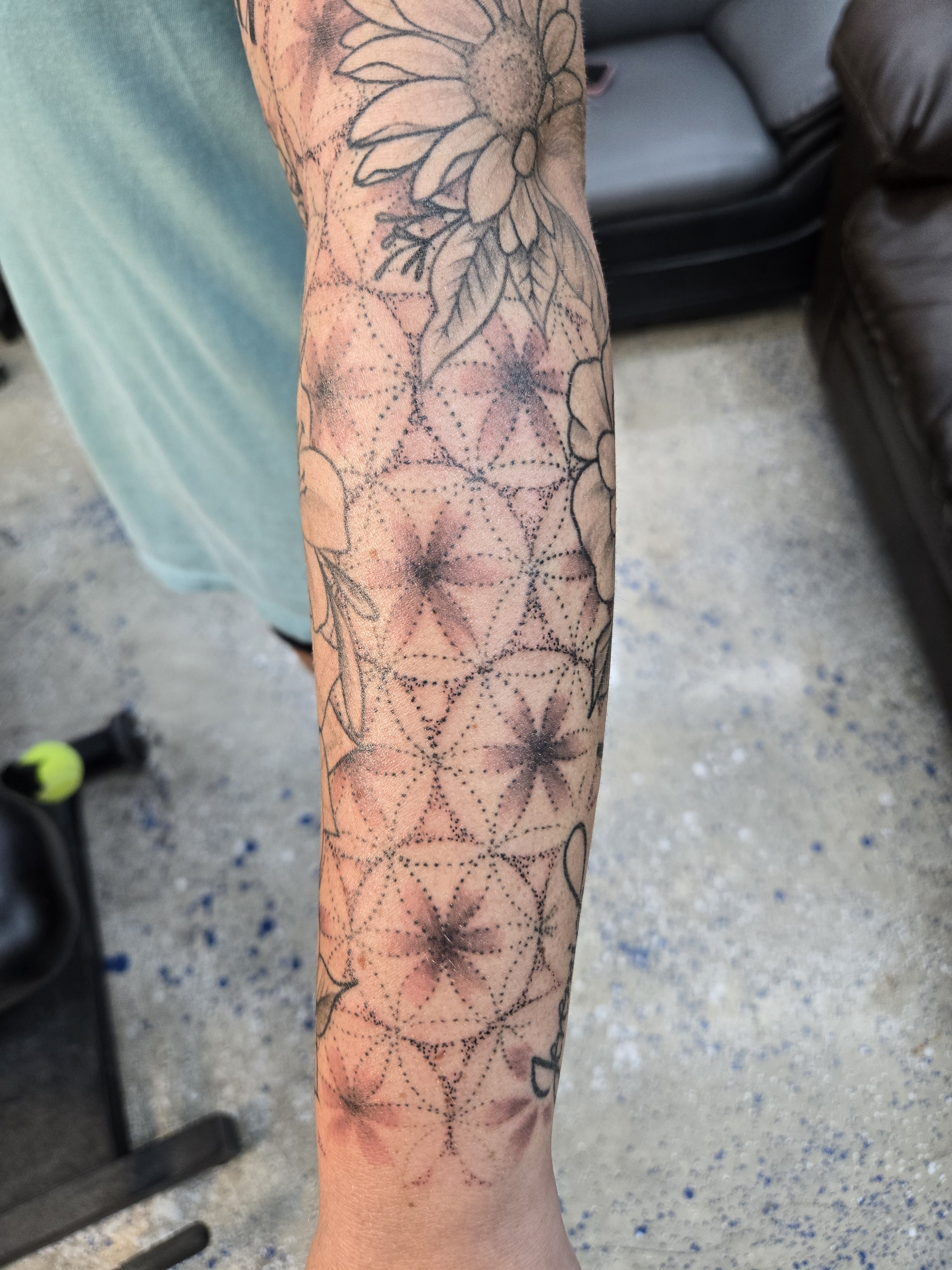 A tattoo sleeve with floral designs and geometric patterns in black ink on a person's arm.