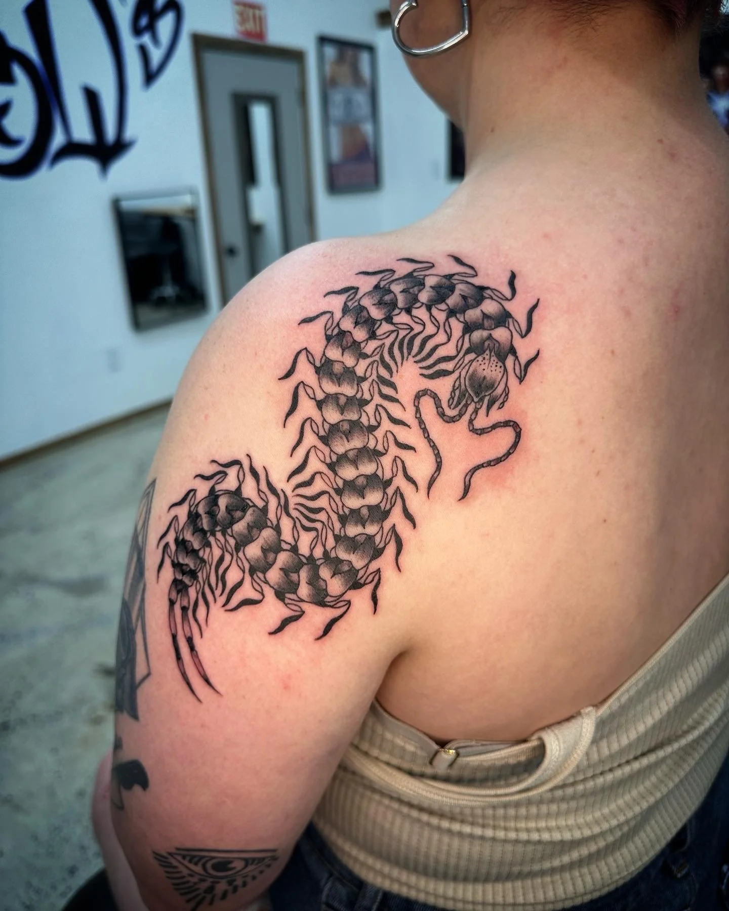 Tattoo of a stylized sea creature, possibly a seahorse or scorpion, with intricate detailing on the person's shoulder.