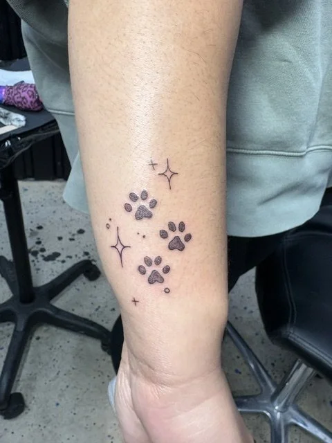 Tattoo of several paw prints and sparkles on a person's inner forearm.