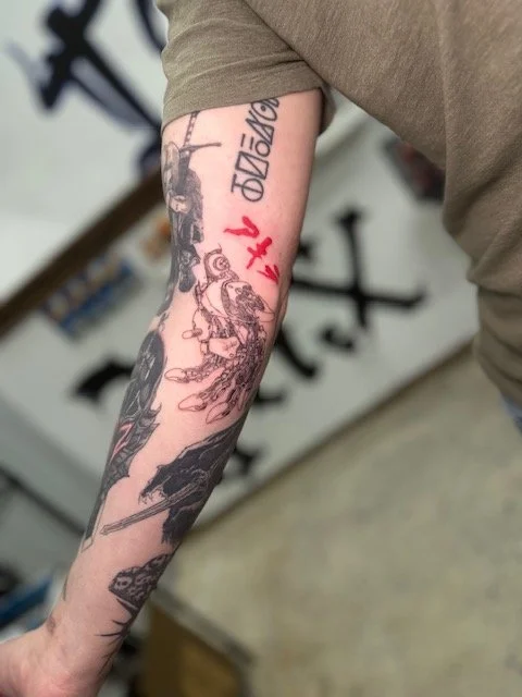 Tattooed arm with various designs including a detailed portrait and script in different colors.