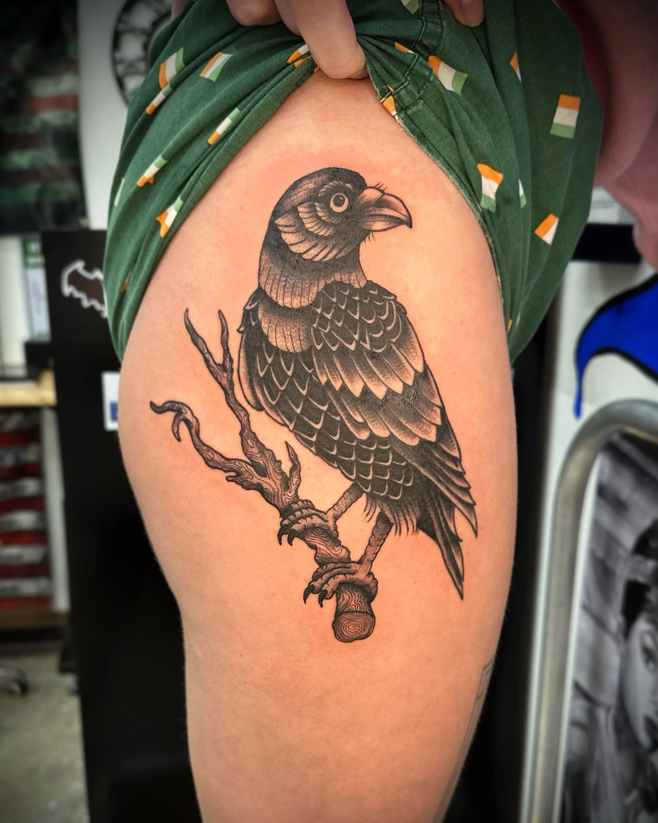 Black and gray tattoo of a bird sitting on a branch on upper arm