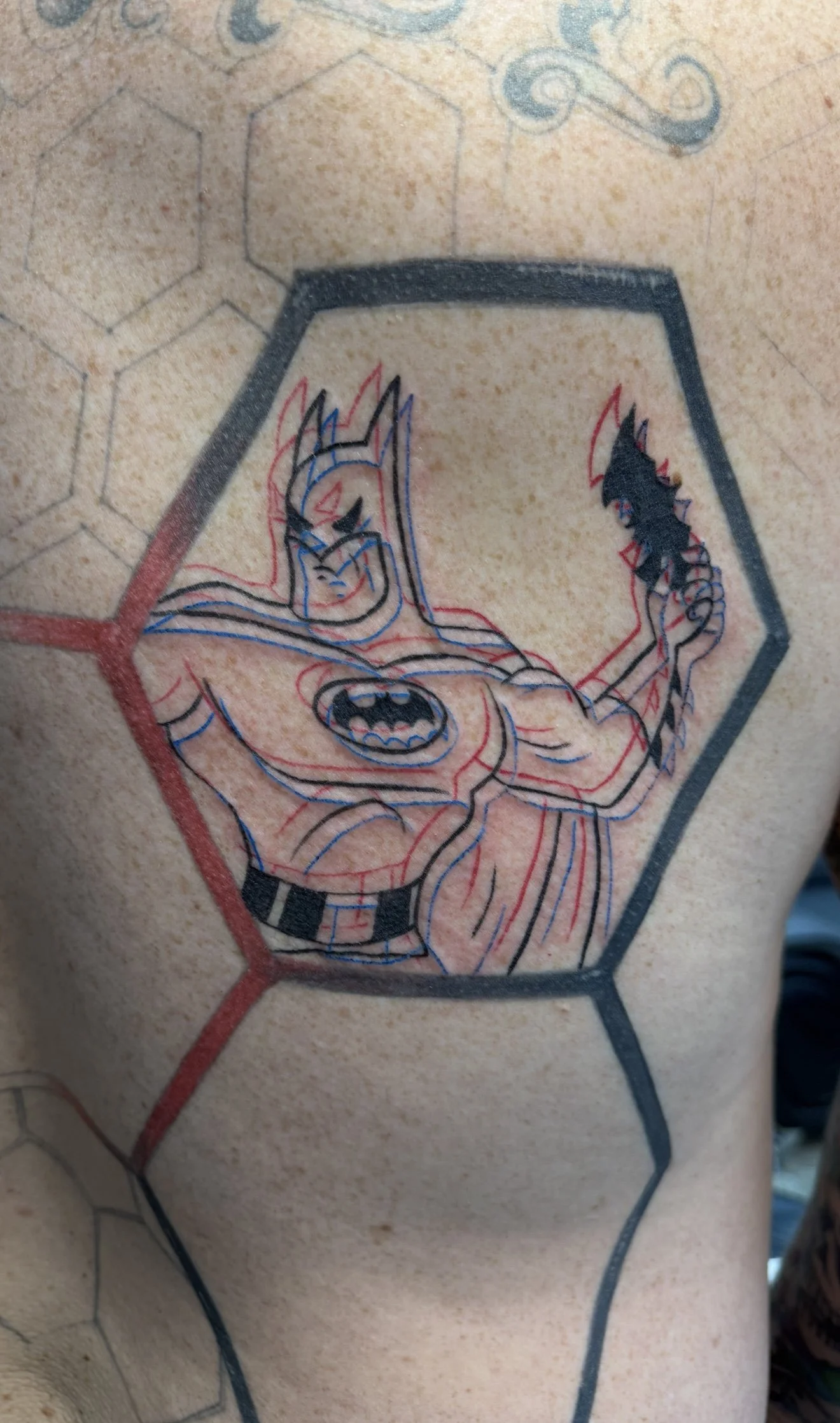Tattoo of Batman with a muscular build inside a hexagon, surrounded by hexagonal patterns.