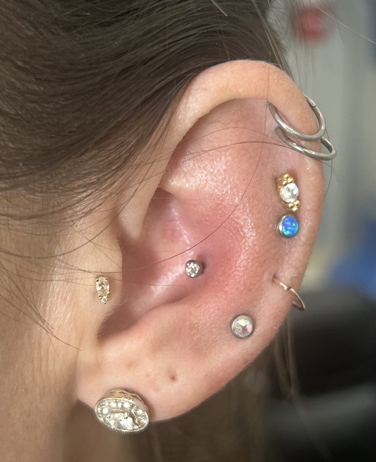 Close-up of a person's ear with multiple earrings, including hoops and studs with various gemstones.