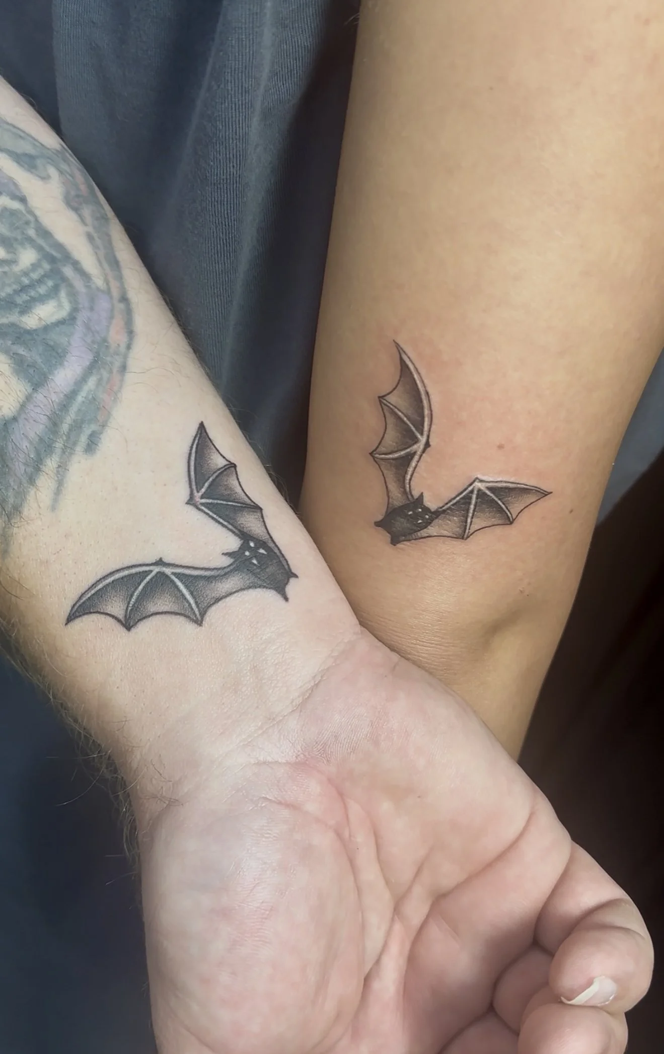 Pair of tattooed arms with matching black and gray bat tattoos on the inner forearms.