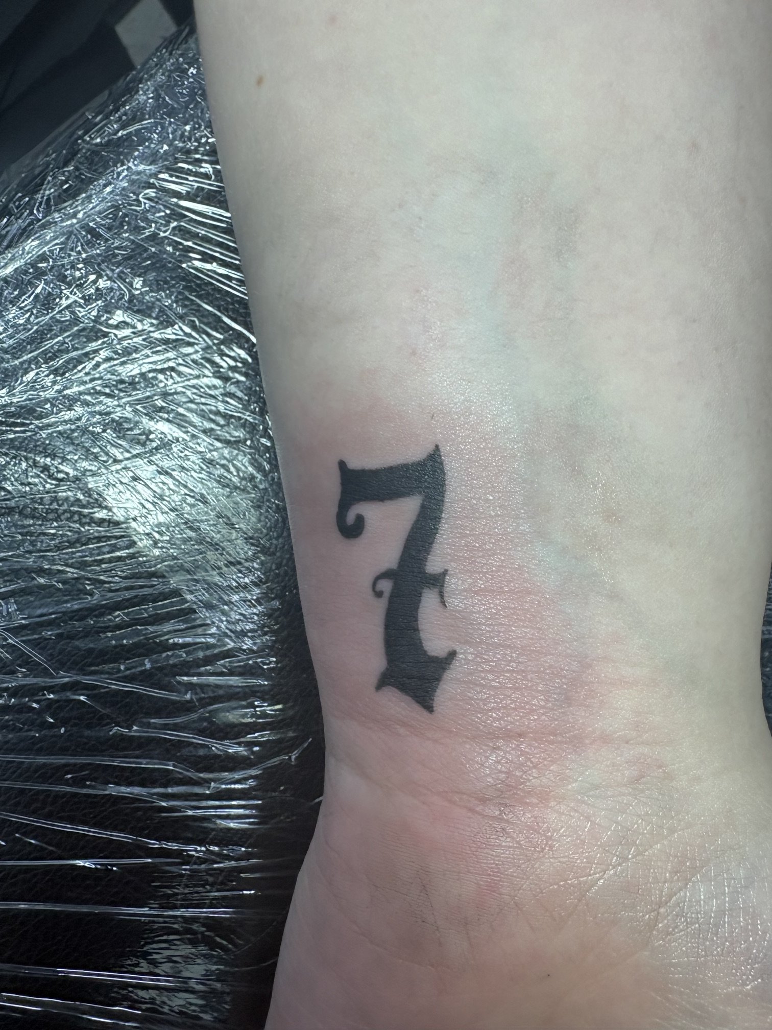 Close-up of a black tattoo letter on a person's skin with a portion of plastic wrap nearby.