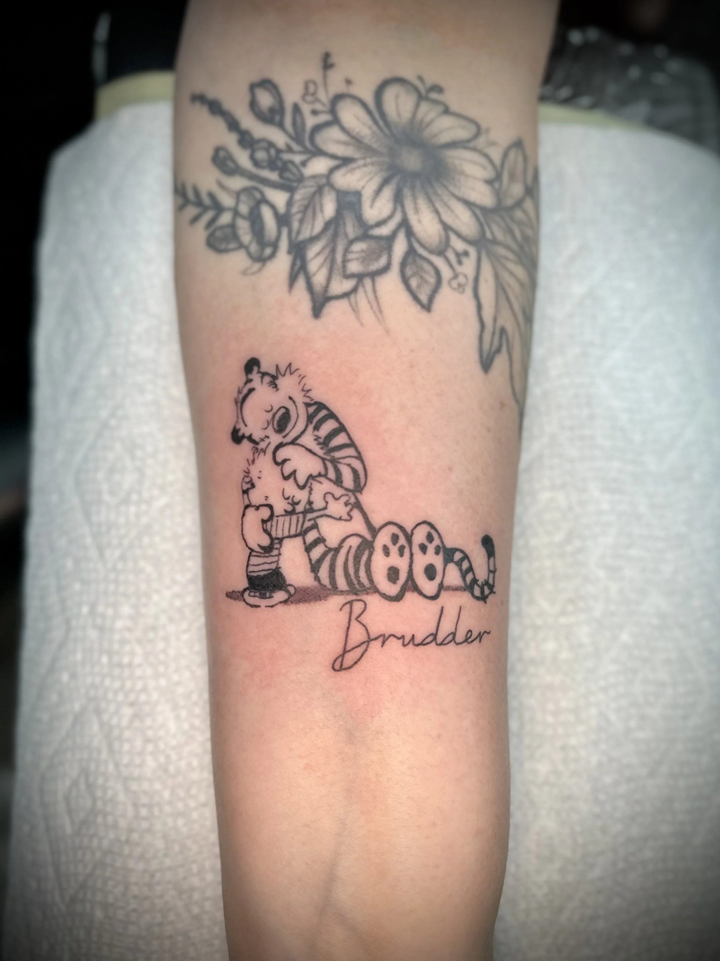 Tattoo of a comic strip character, Calvin from Calvin and Hobbes, sitting with a sad expression, with the word 'Brudder' written below.
