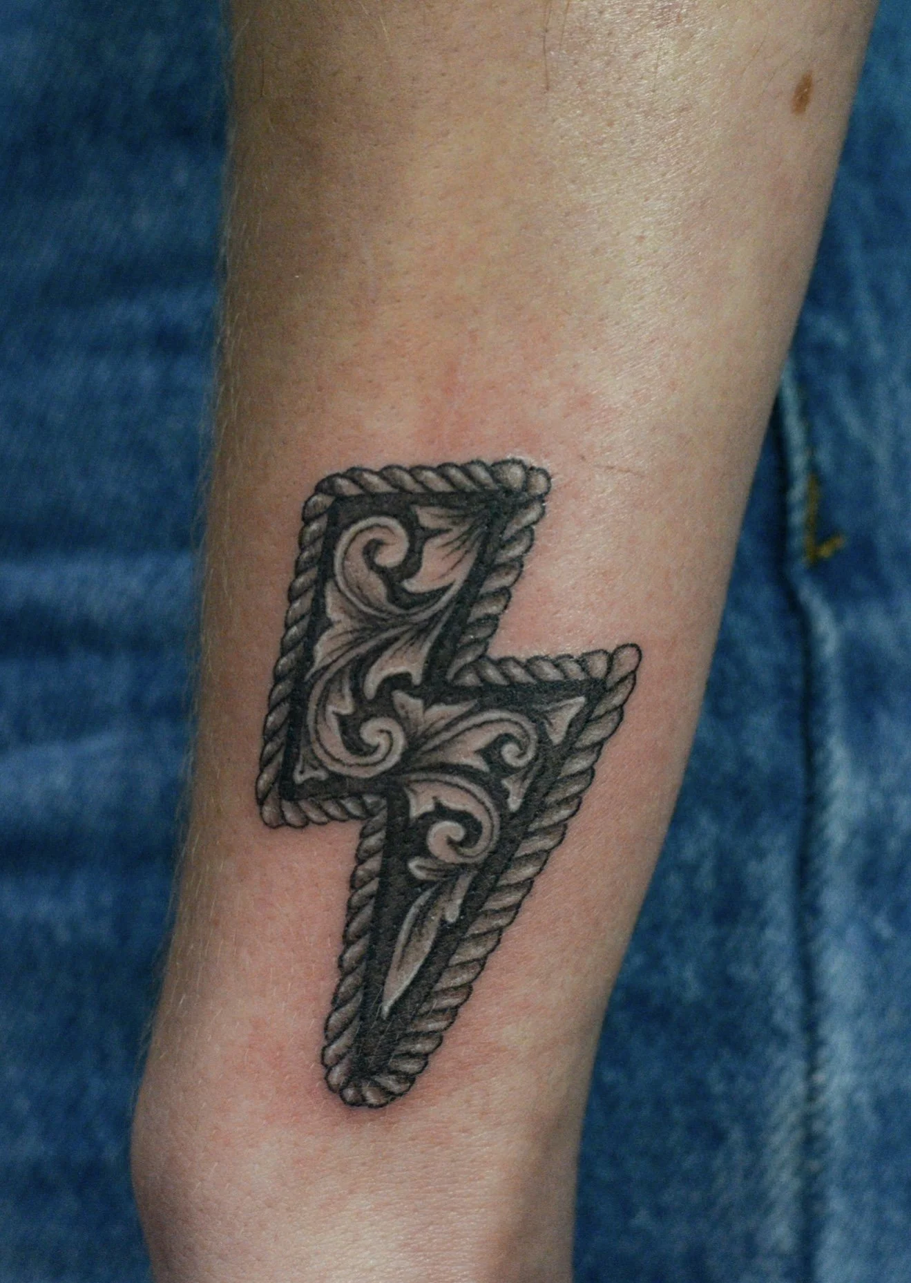 A tattoo of the number 7 featuring ornate, decorative shading and a rope border, tattooed on a person's forearm.