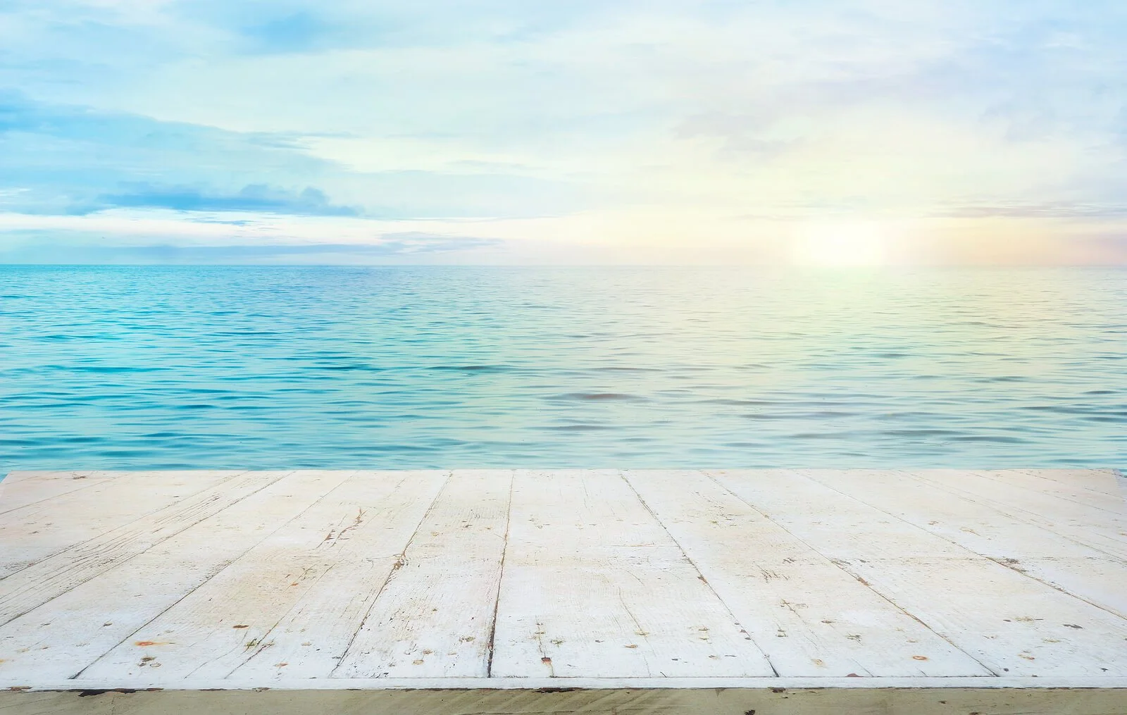 A weathered white wooden dock extending toward a calm, sunlit ocean under a soft blue sky. Is contamination OCD keeping you from enjoying peaceful, everyday moments like this? An OCD therapist in Wauwatosa, WI, can help you reclaim them.