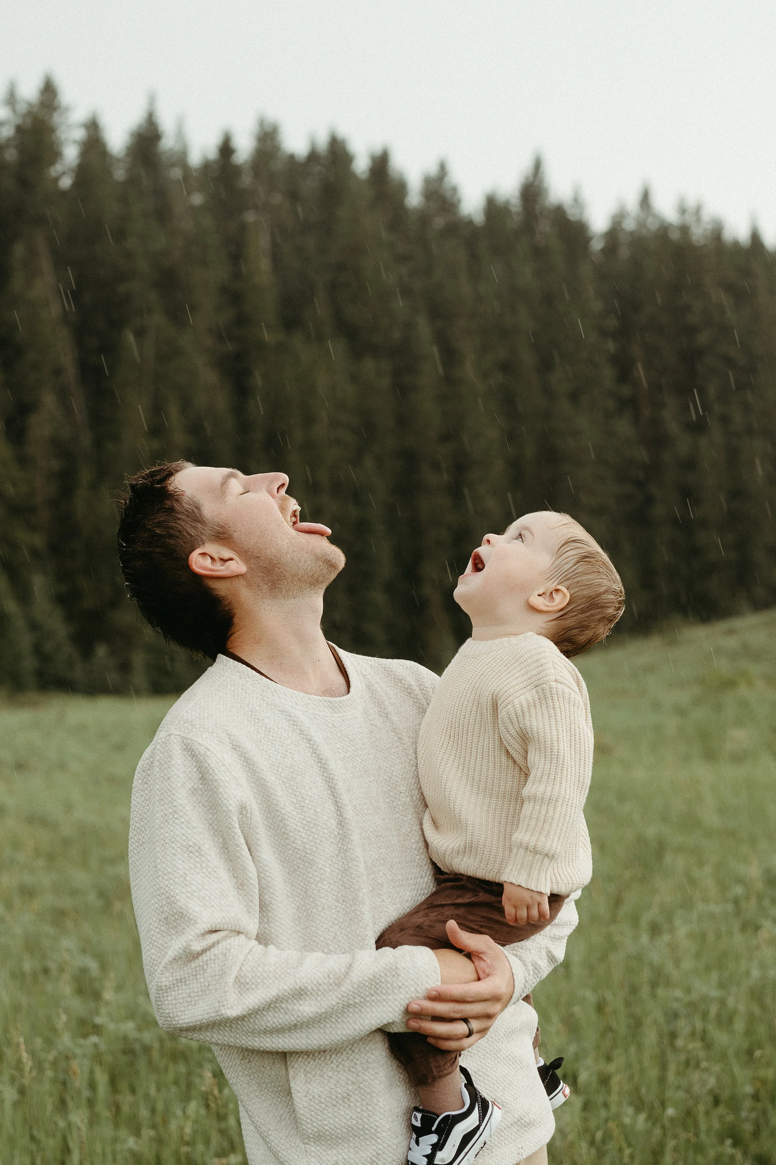 Calgary Alberta Family Photographer.  Dad with Son playing in the rain in the forest