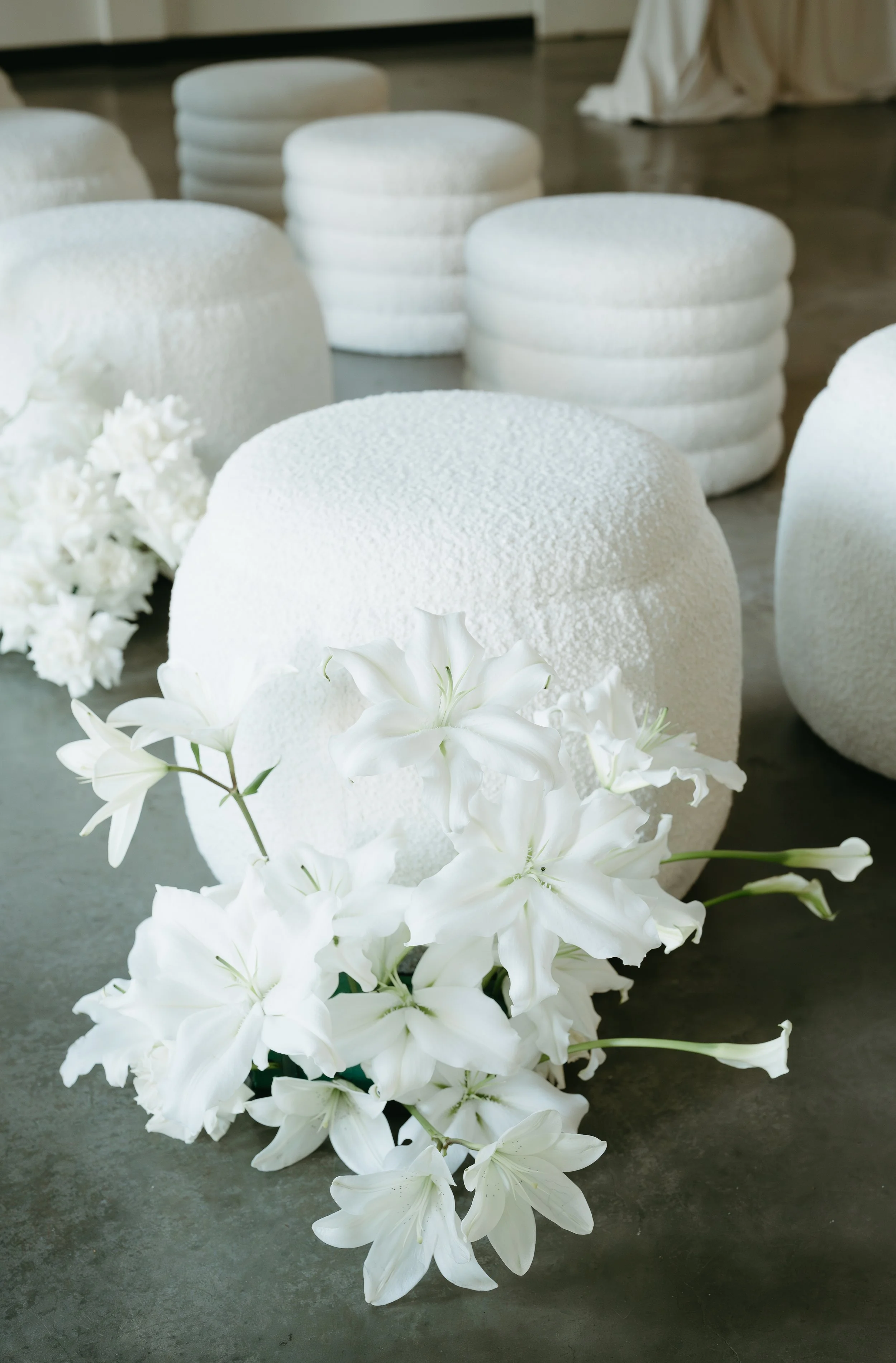 Two rows of white wedding stools with bouquets of white flowers laid on the ground beside them. July 2025 Calgary Elopement/Wedding Editorial Session with KC Photography