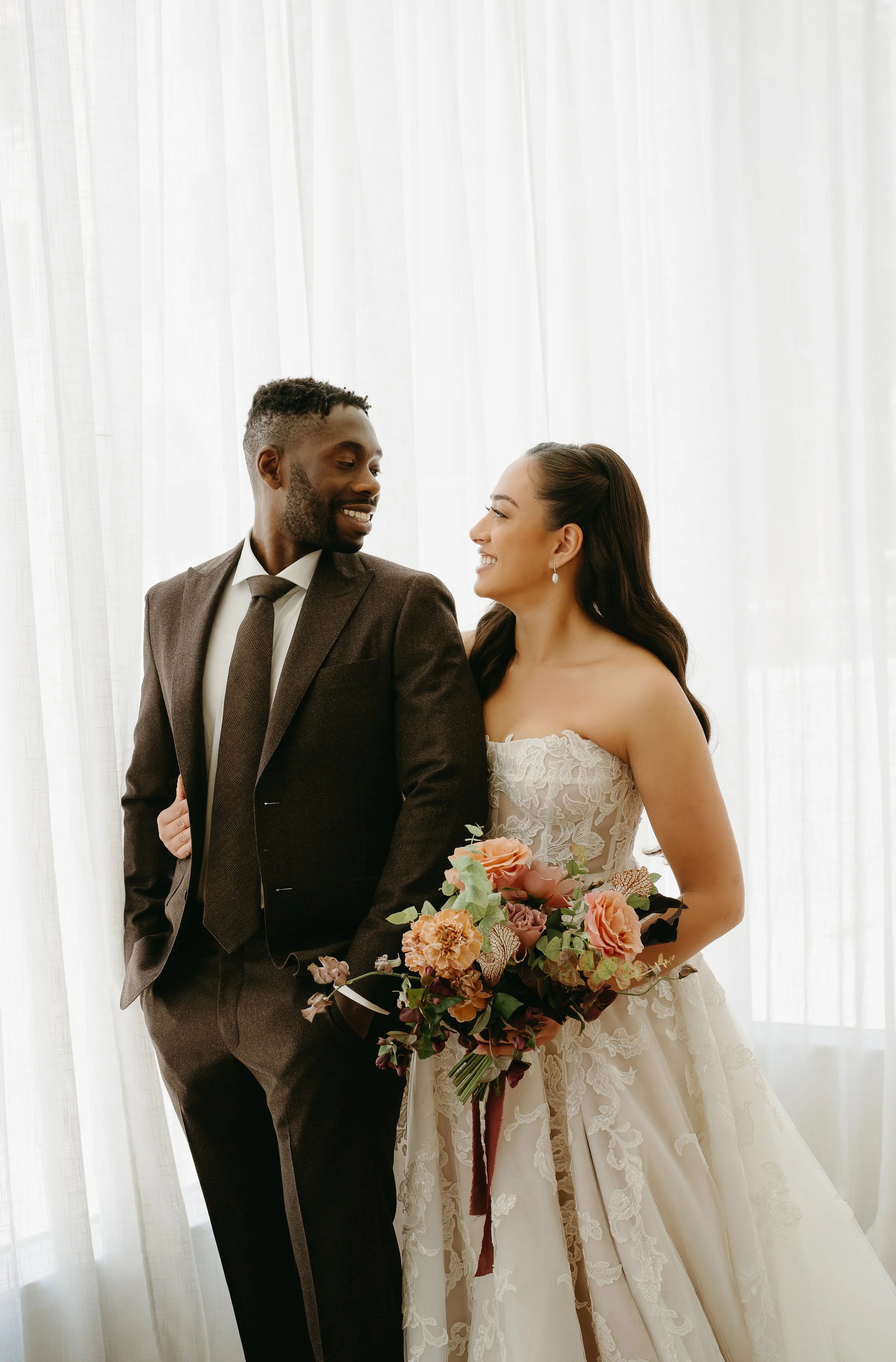 A bride wraps her arm around her groom as they stand side by side looking at one another smiling. July 2025 Calgary Elopement/Wedding Editorial Session with KC Photography