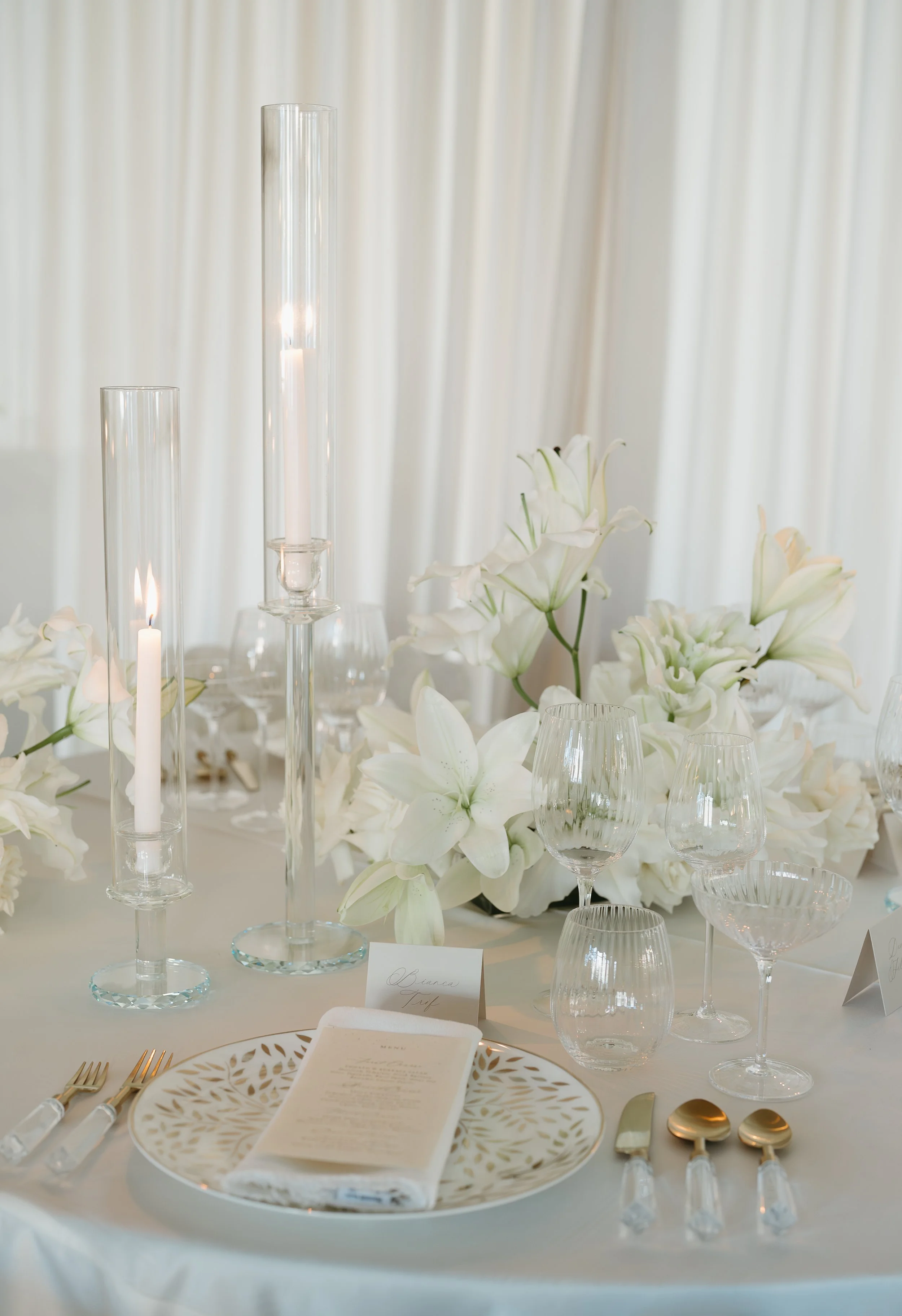 The tabletop of a wedding reception covered with table arrangements, white lily's, and candles. July 2025 Calgary Elopement/Wedding Editorial Session with KC Photography