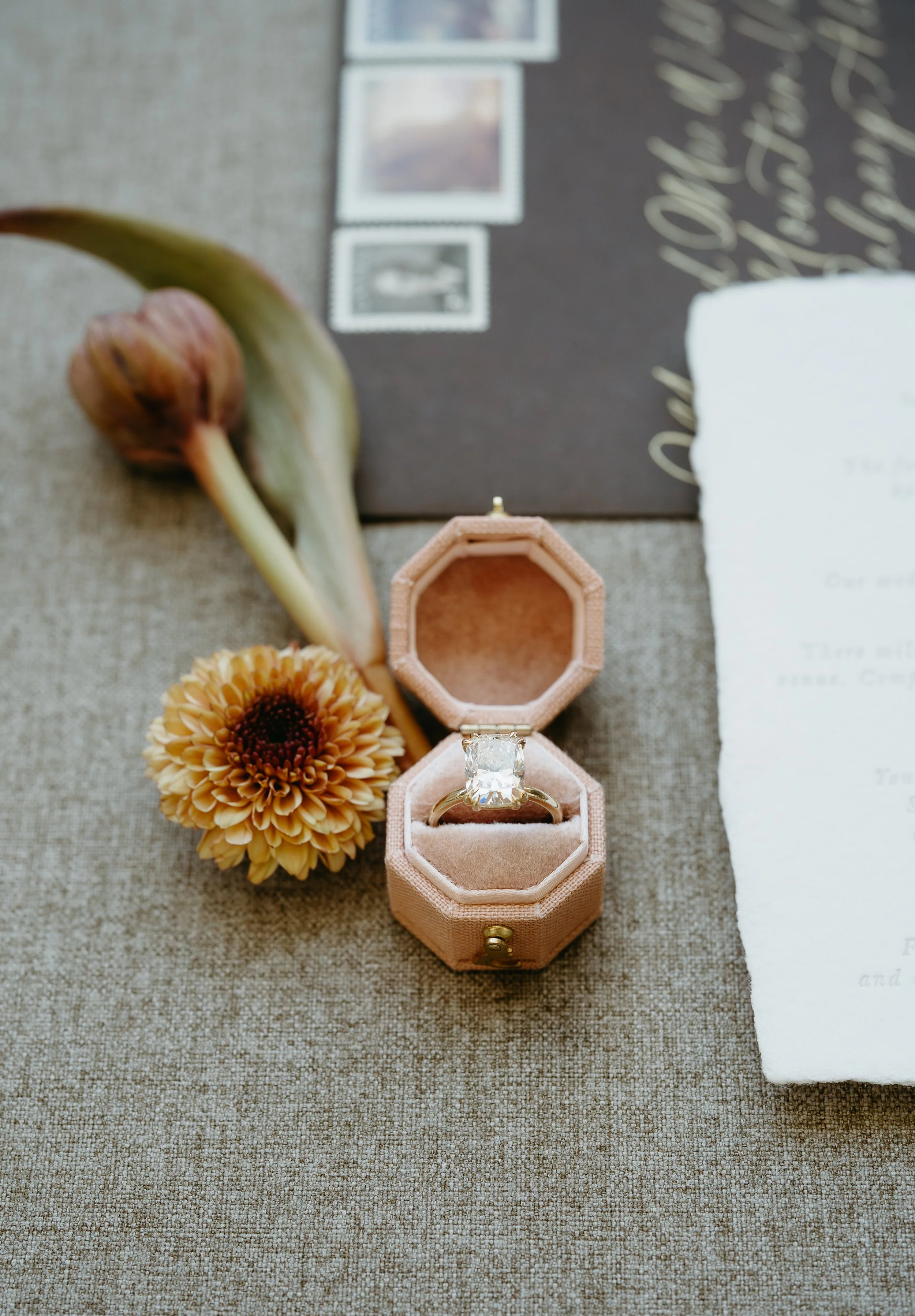 A wedding band is placed on a grey surface surrounded by flowers and wedding invitations. July 2025 Calgary Elopement/Wedding Editorial Session with KC Photography