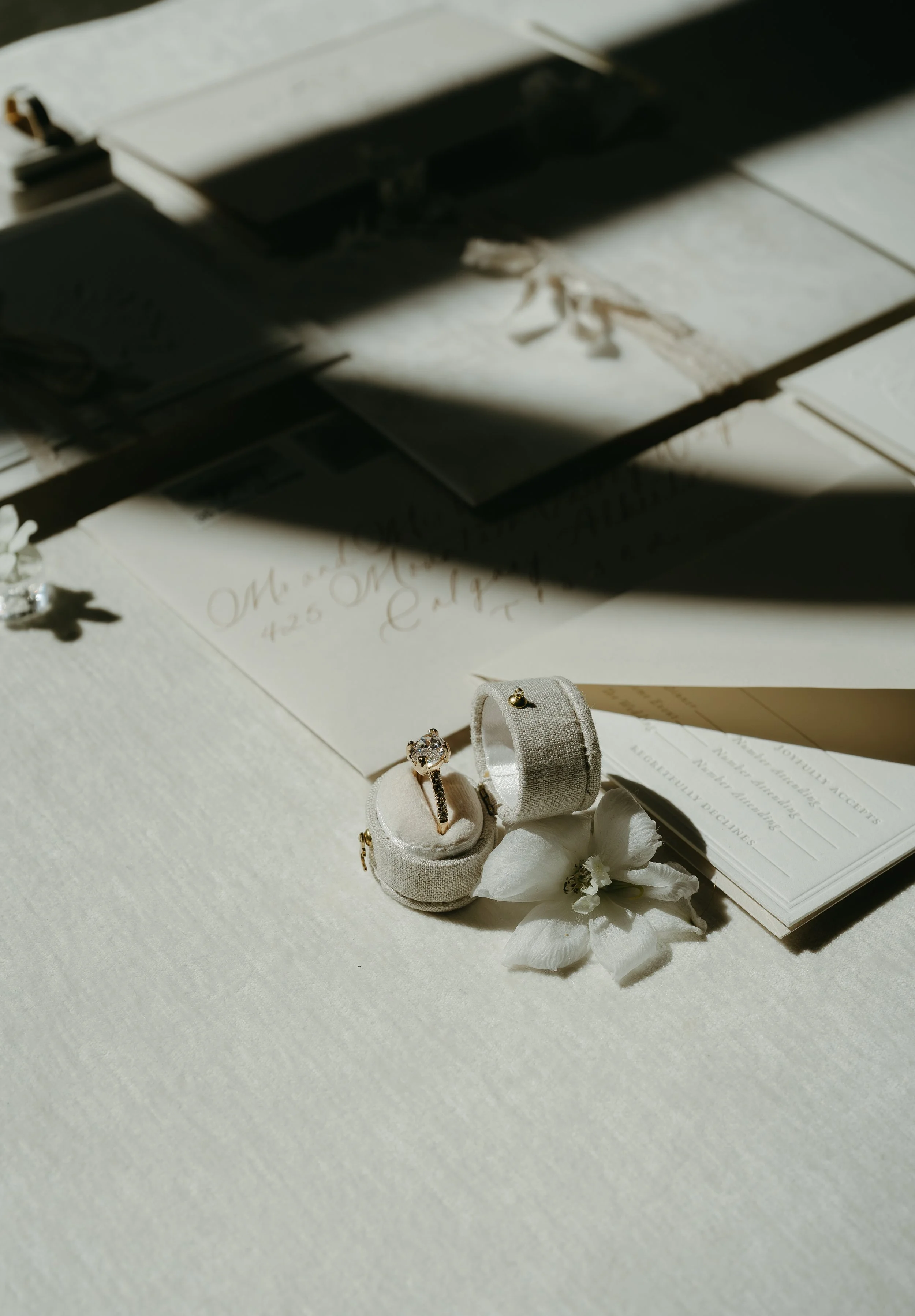 Wedding invitations and a wedding band laid out on a white surface. July 2025 Calgary Elopement/Wedding Editorial Session with KC Photography