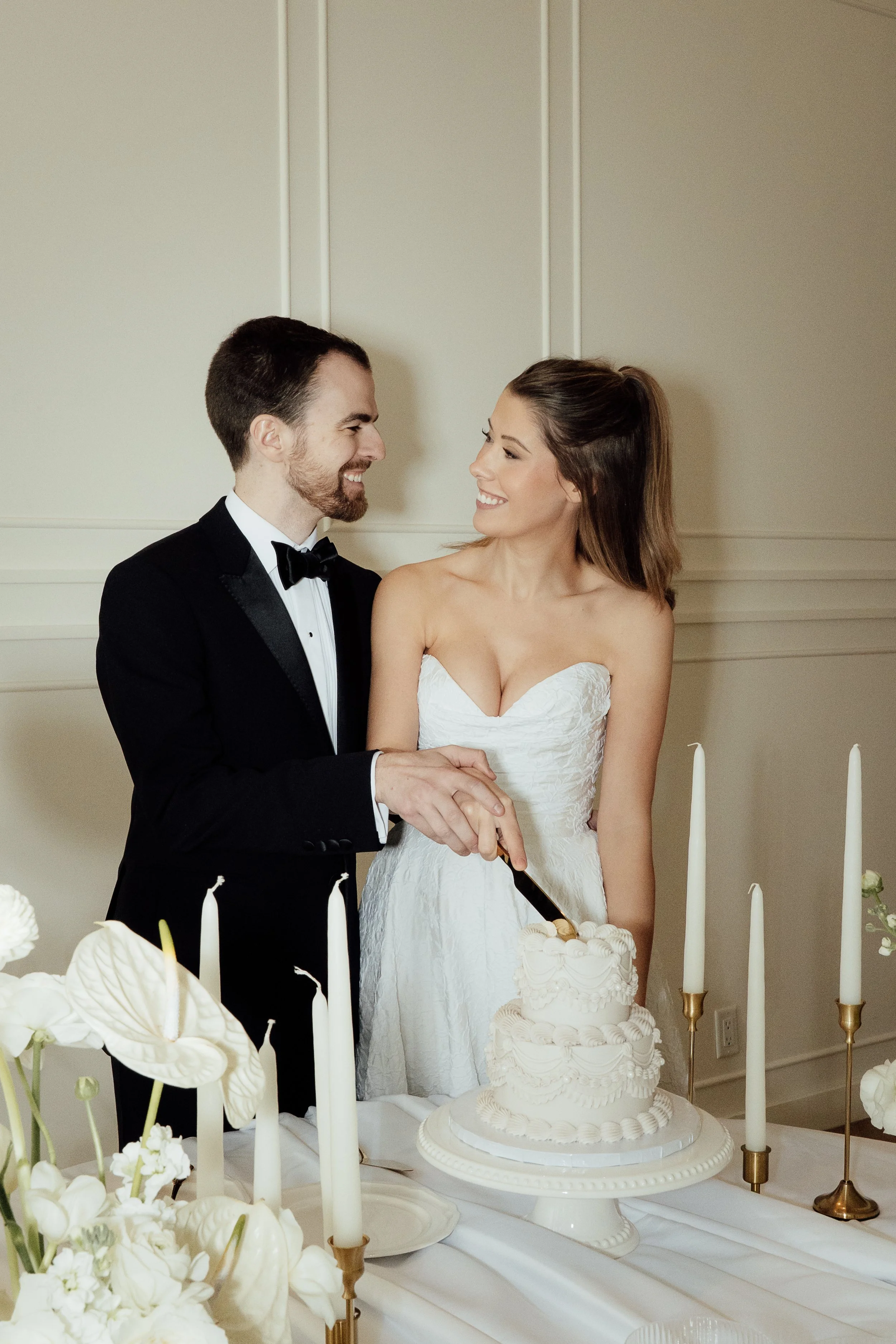 A bride and groom look at each other smiling as they cut into their wedding cake. Calgary Elopement/Wedding Editorial Session with KC Photography