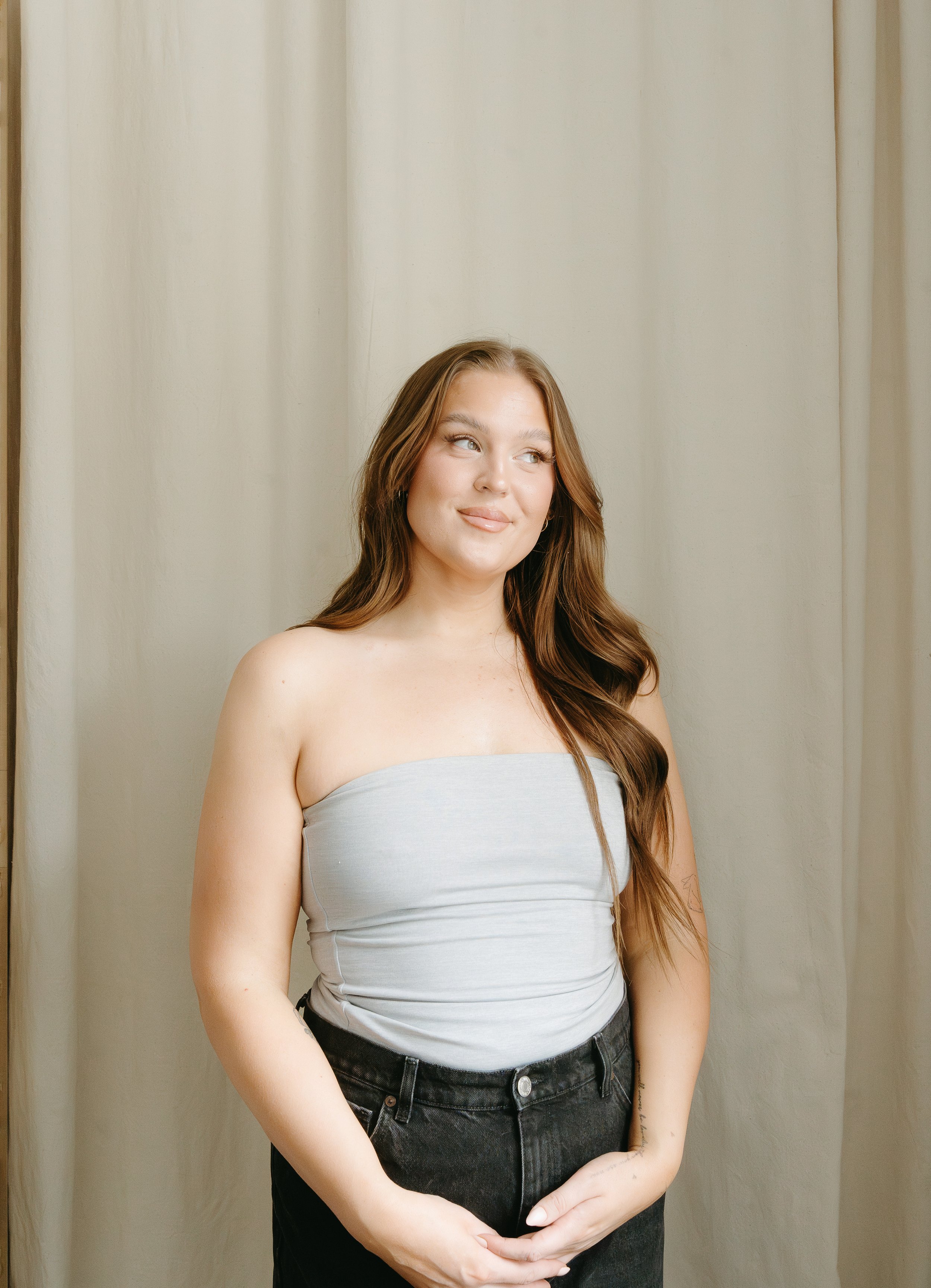 A woman stands holding her hands and smiling as she looks into the distance. Beauty Ave Studio Branding Session with KC Photography