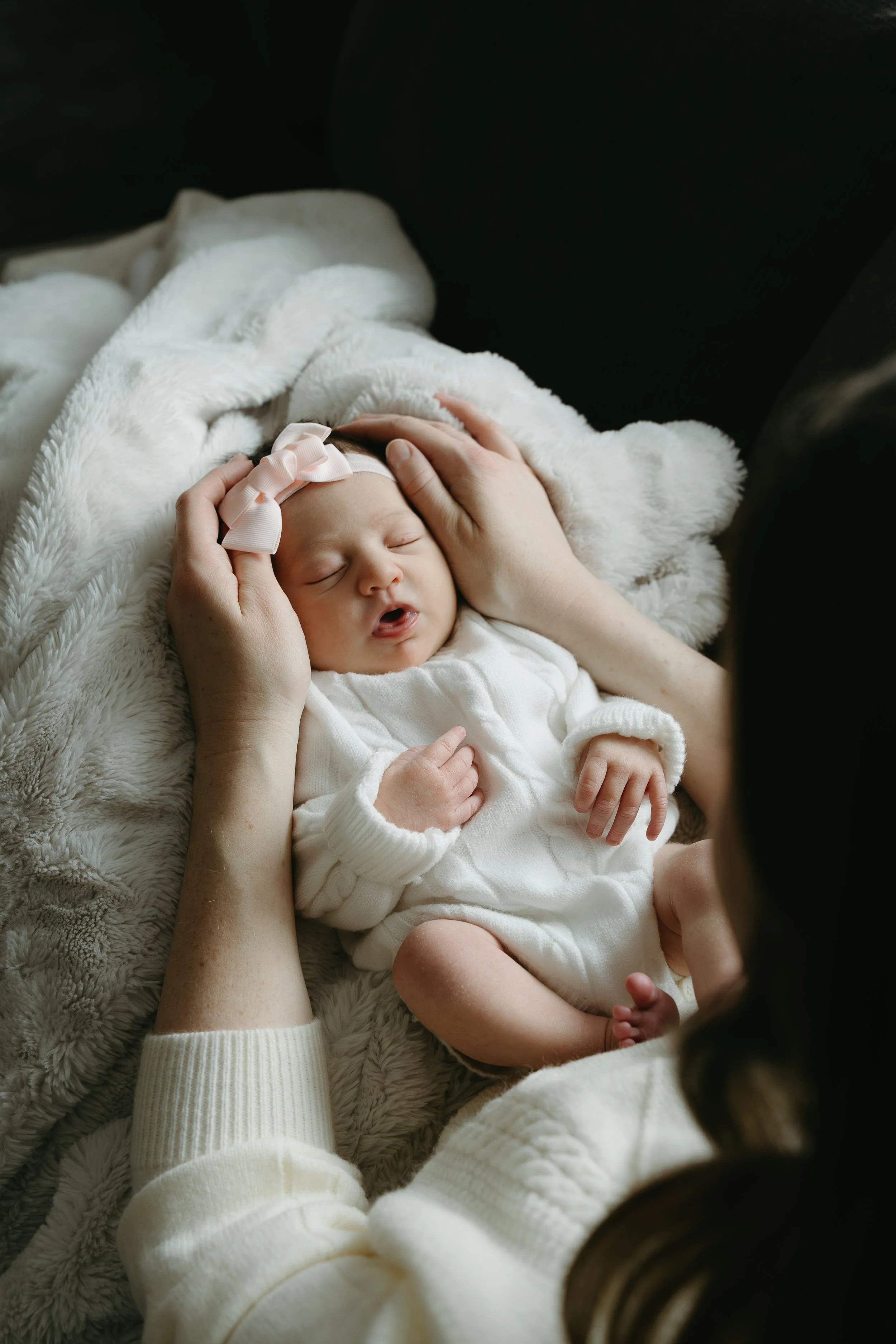 An over the shoulder shot of a mother who is sat looking down at her newborn who is laying in her lap. Calgary Home Lifestyle/Family/Newborn Session with KC Photography