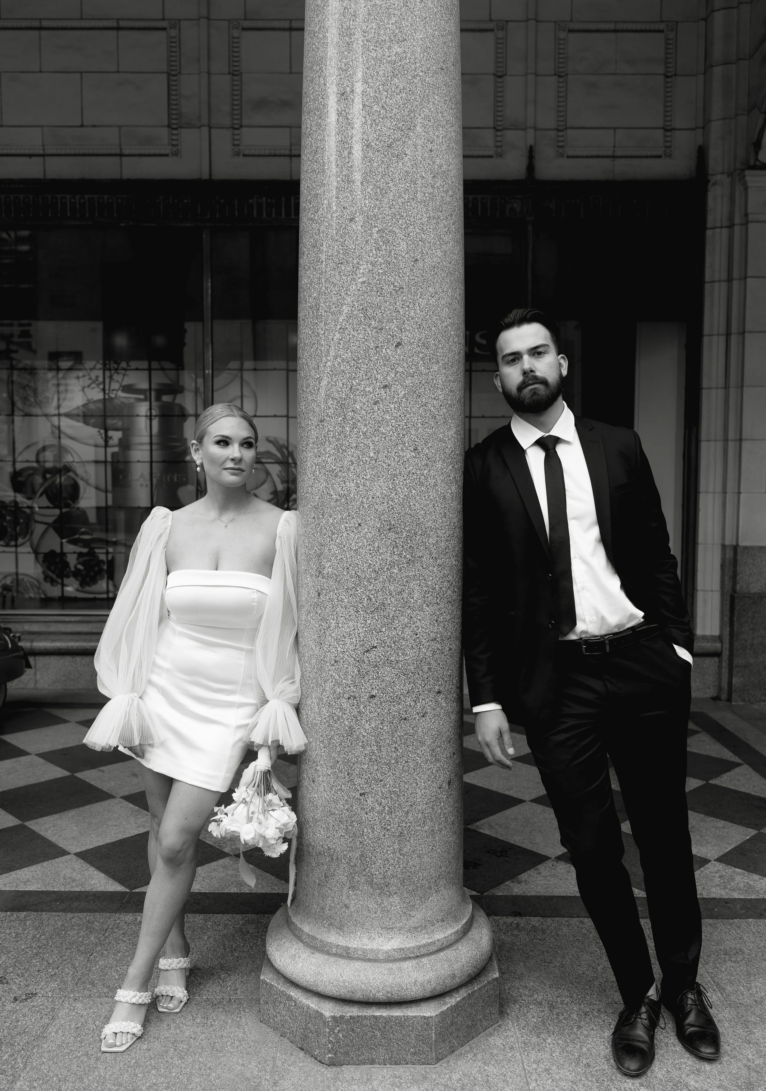 A bride and groom rest on either side of a pillar in Downtown Calgary. Downtown Calgary Elopement/Wedding Session with KC Photography