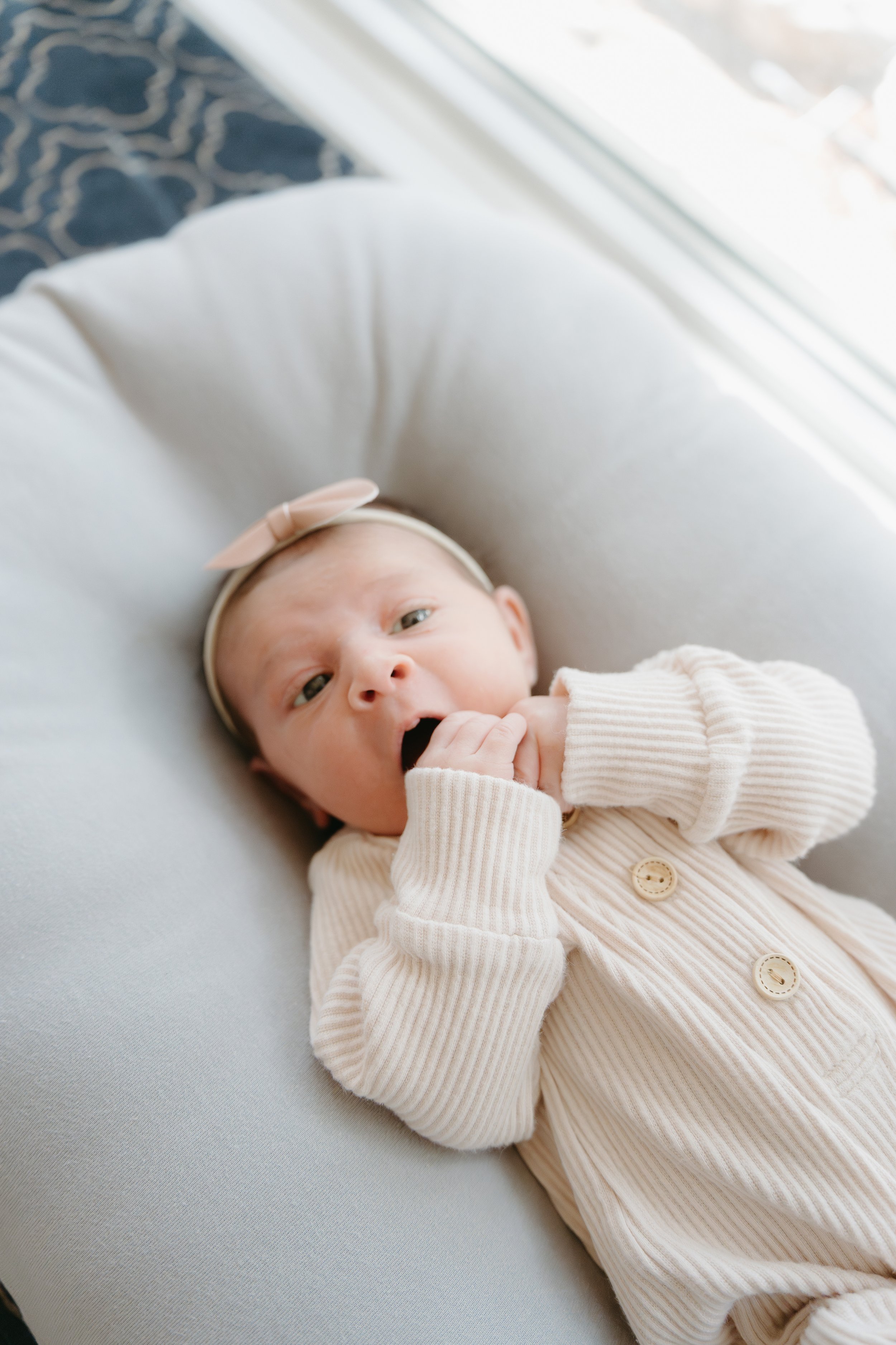 A newborn baby lays on a grey pillow looking up at the camera. Calgary Lifestyle/Family/Newborn Home Session with KC Photography