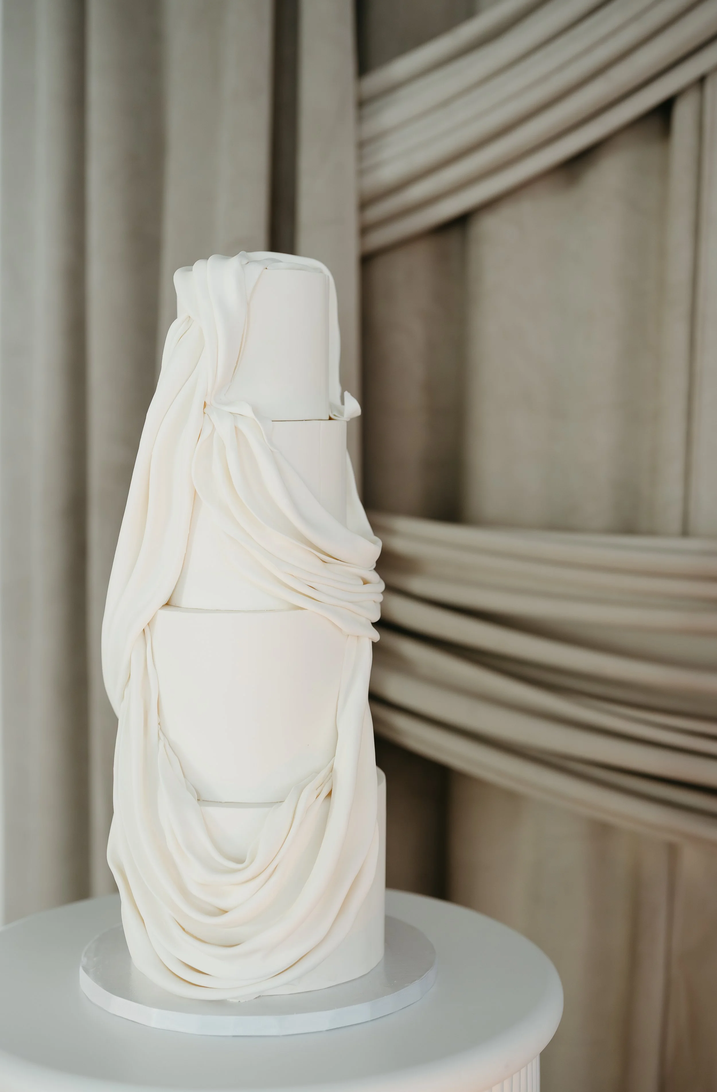 A white teared wedding cake sits untouched on a small table.July 2025 Calgary Elopement/Wedding Editorial Session with KC Photography