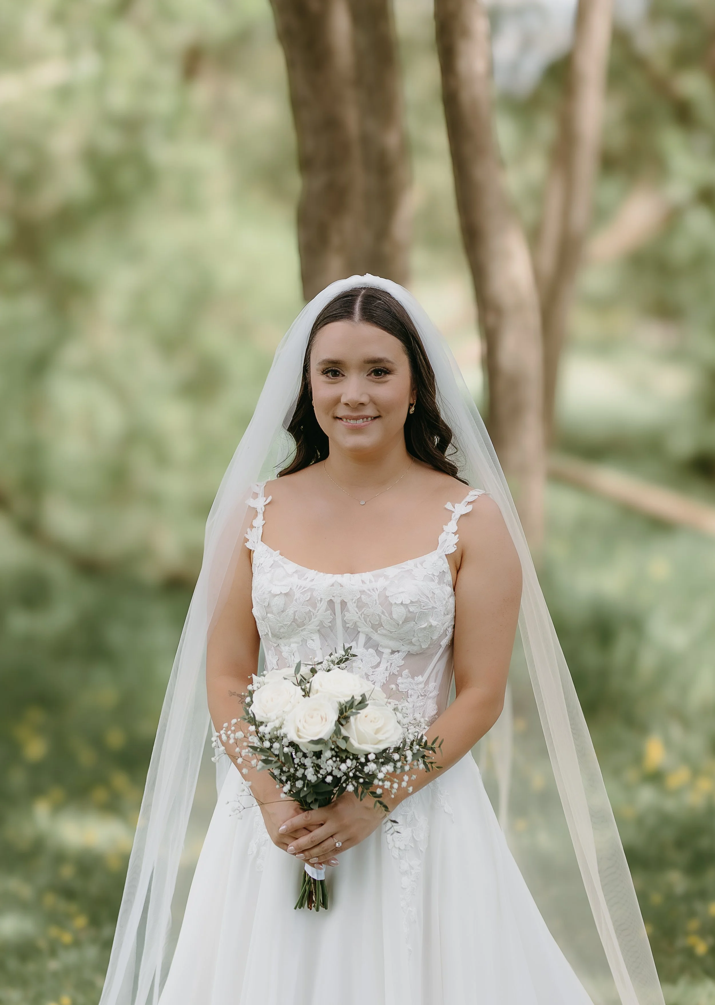A bride holds her bouquet of flowers smiling while wearing her wedding gown. Jessica and Devon May 2025 Wedding Photography Session with KC Photography