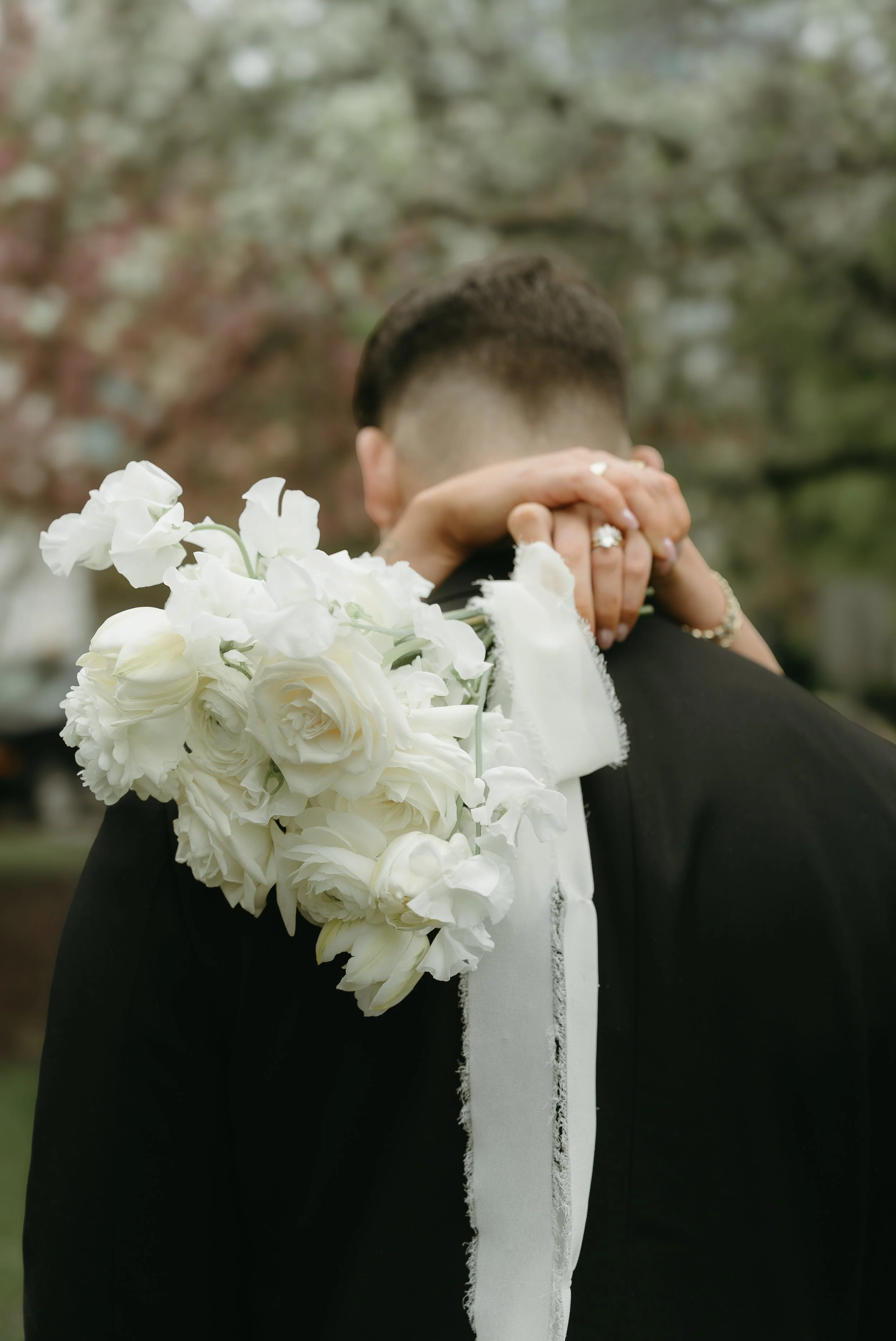 A photo of arms wrapped around the back of a man holding a bouquet of wedding flowers. Downtown Calgary Elopement/Wedding Session with KC Photography