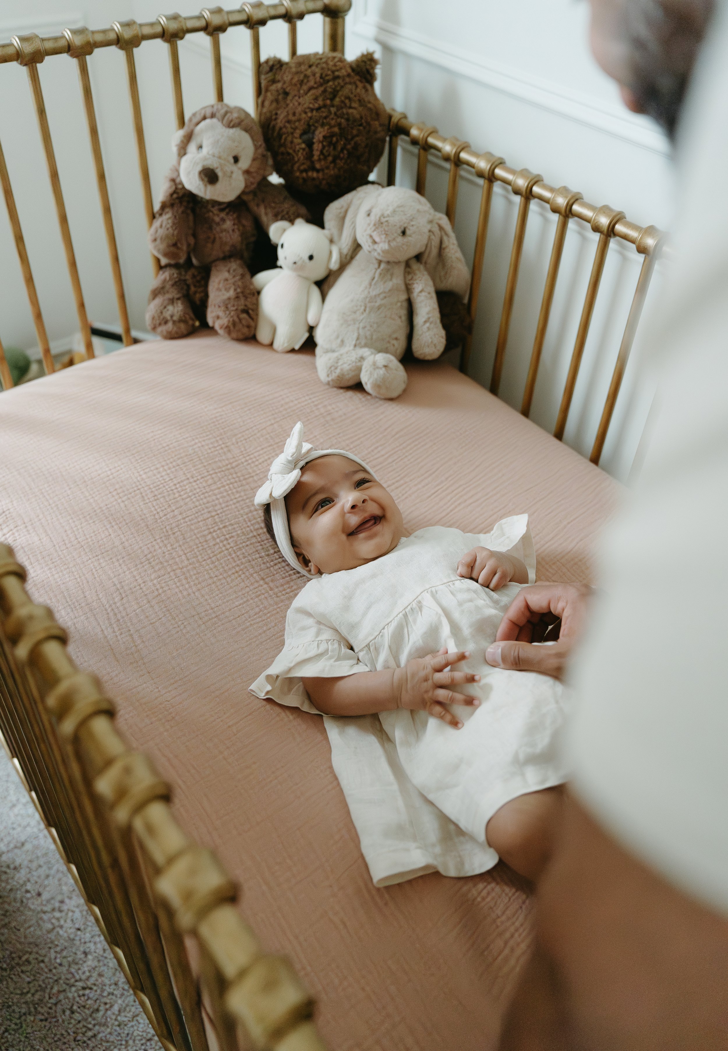 An over the shoulder shot of a father reaching into a crib to tickle his newborn who is laughing and smiling as they look up at him. Calgary Lifestyle/Family/Newborn/Pregnancy/Maternity Studio Session with KC Photography