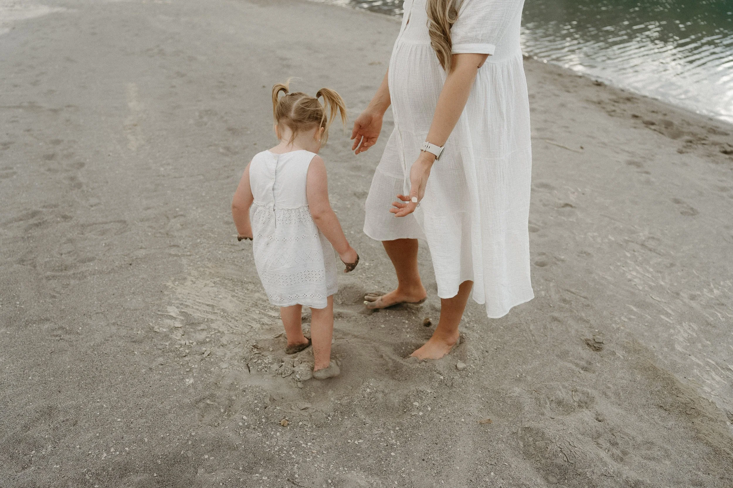 A woman and her toddler standing barefoot while they play in the sand. Canmore/Banff Lifestyle/Family Session with KC Photography