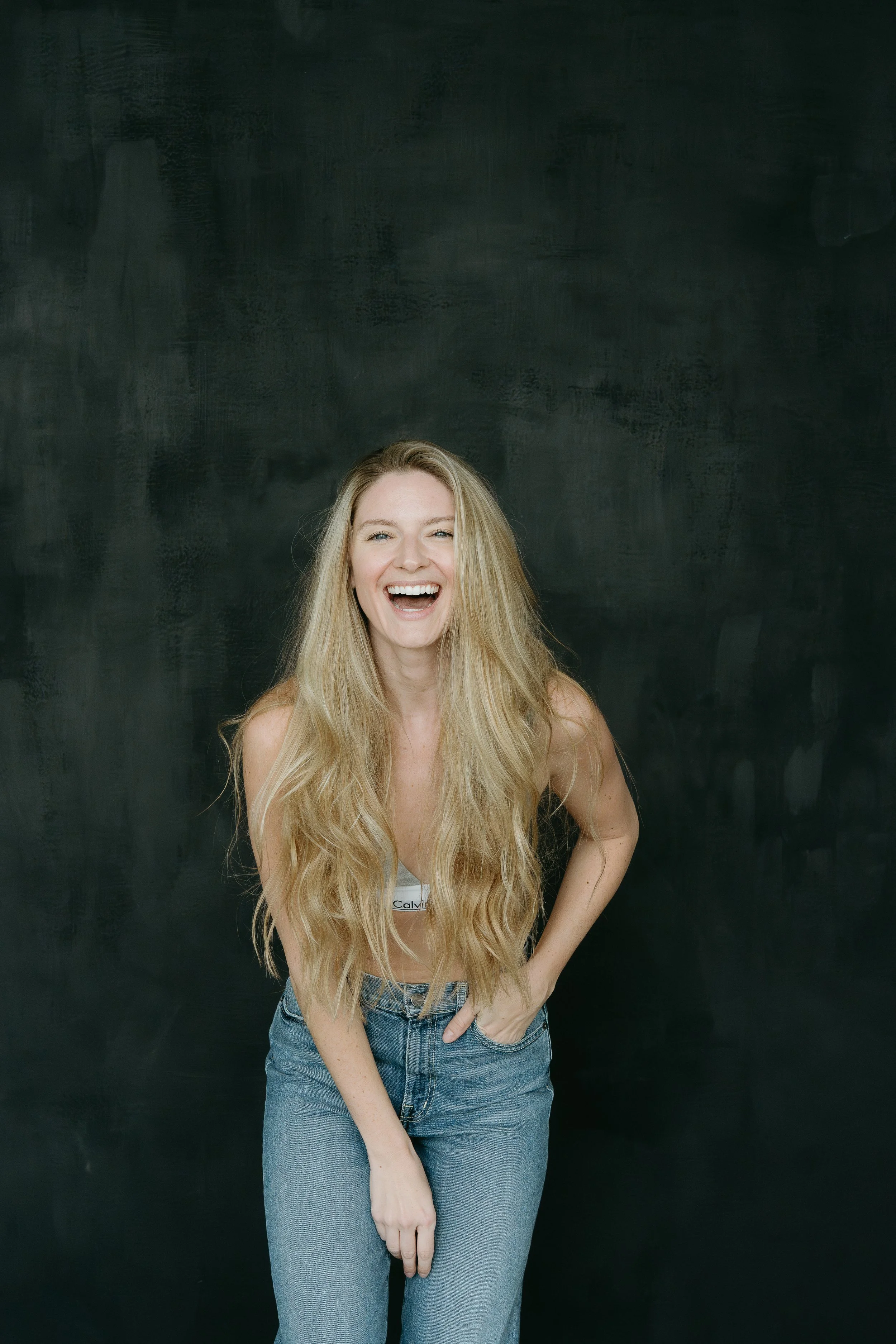 A woman stands on a dark backdrop and looks into the camera as she laughs. Calgary Studio Branding Session with KC Photography
