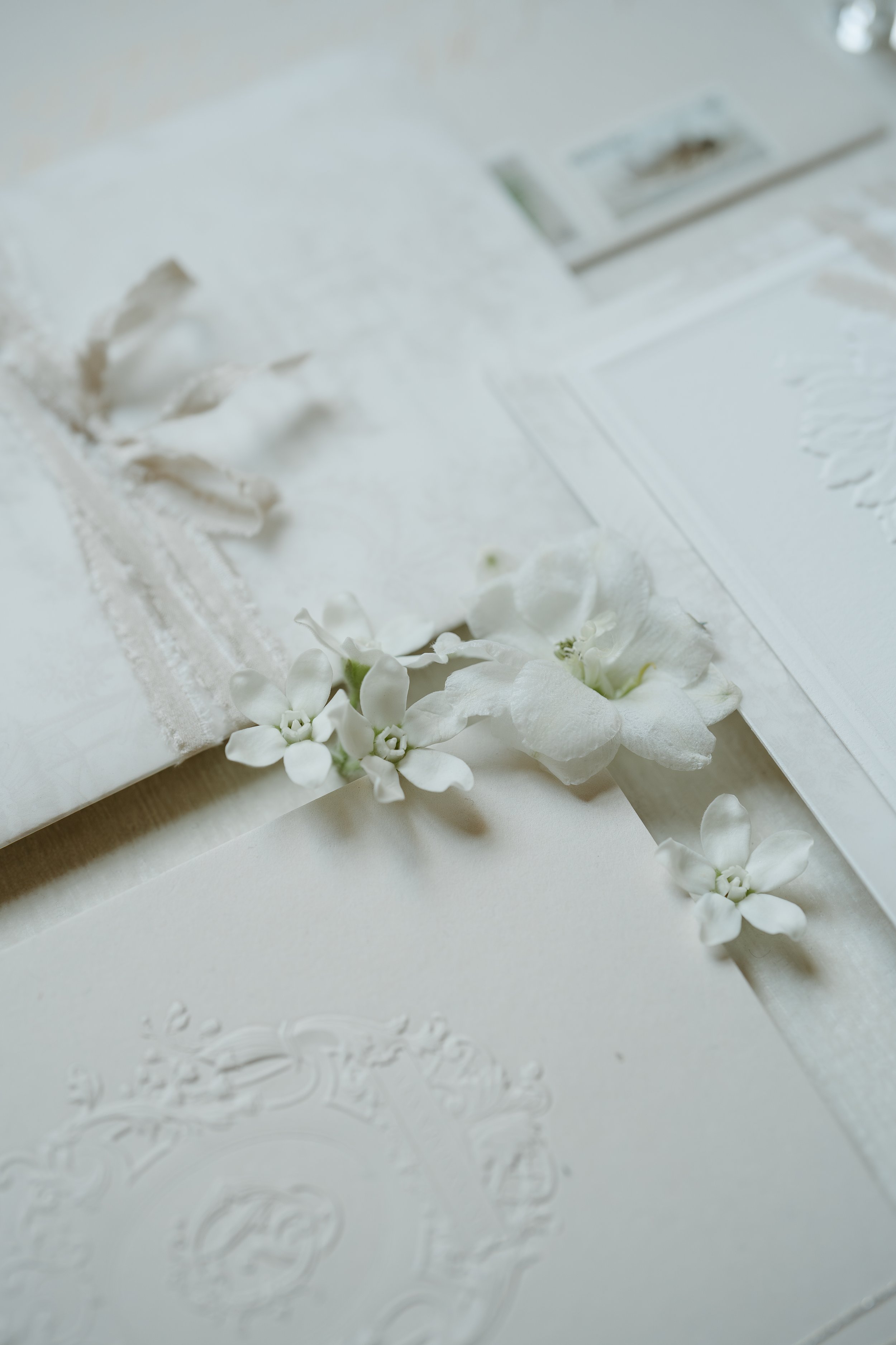 Wedding invitations laid out on a white surface with white flowers filling the gaps between them. July 2025 Calgary Elopement/Wedding Editorial Session with KC Photography