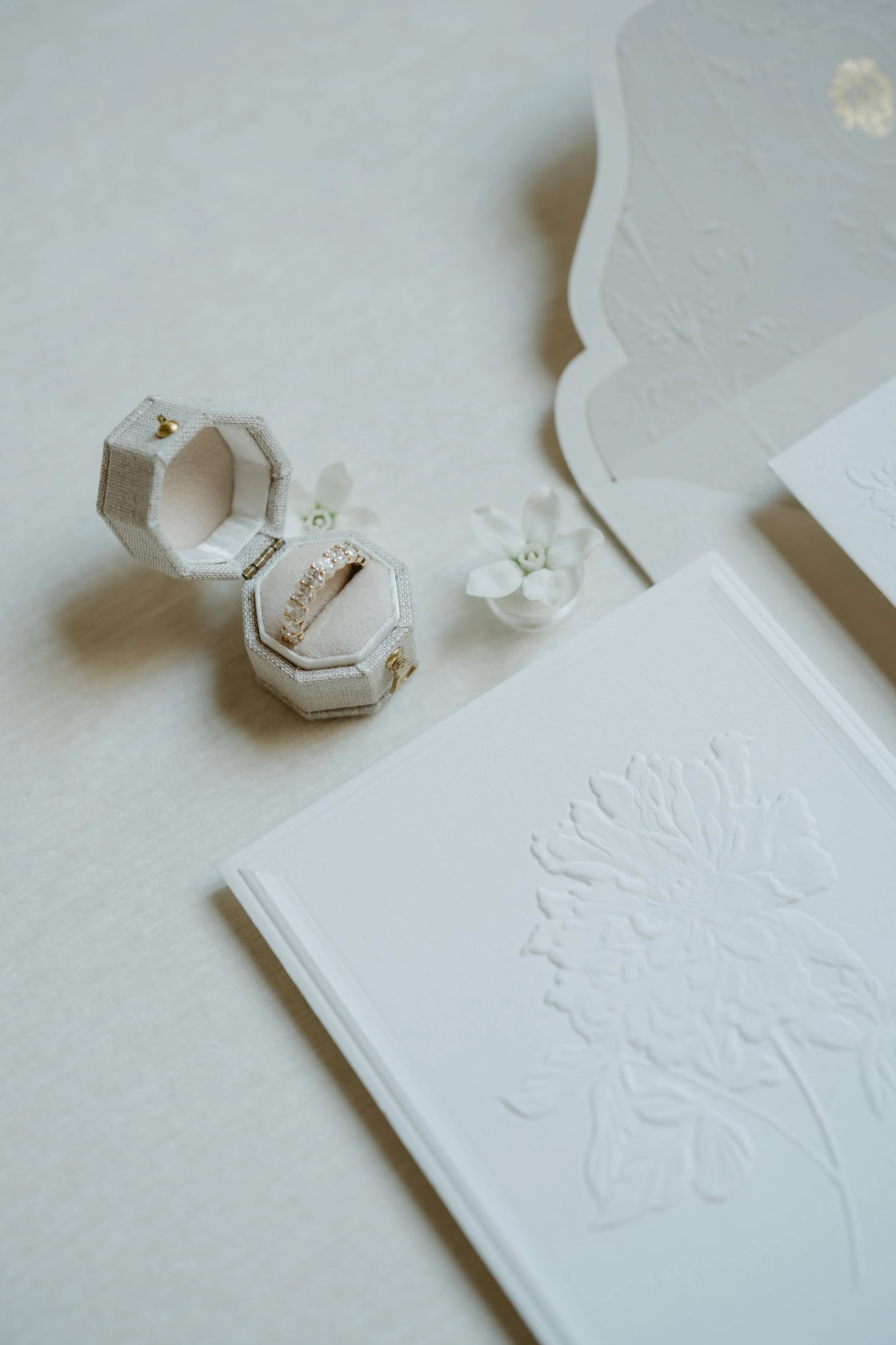 Wedding invitations and a wedding band laid out on a white surface. July 2025 Calgary Elopement/Wedding Editorial Session with KC Photography