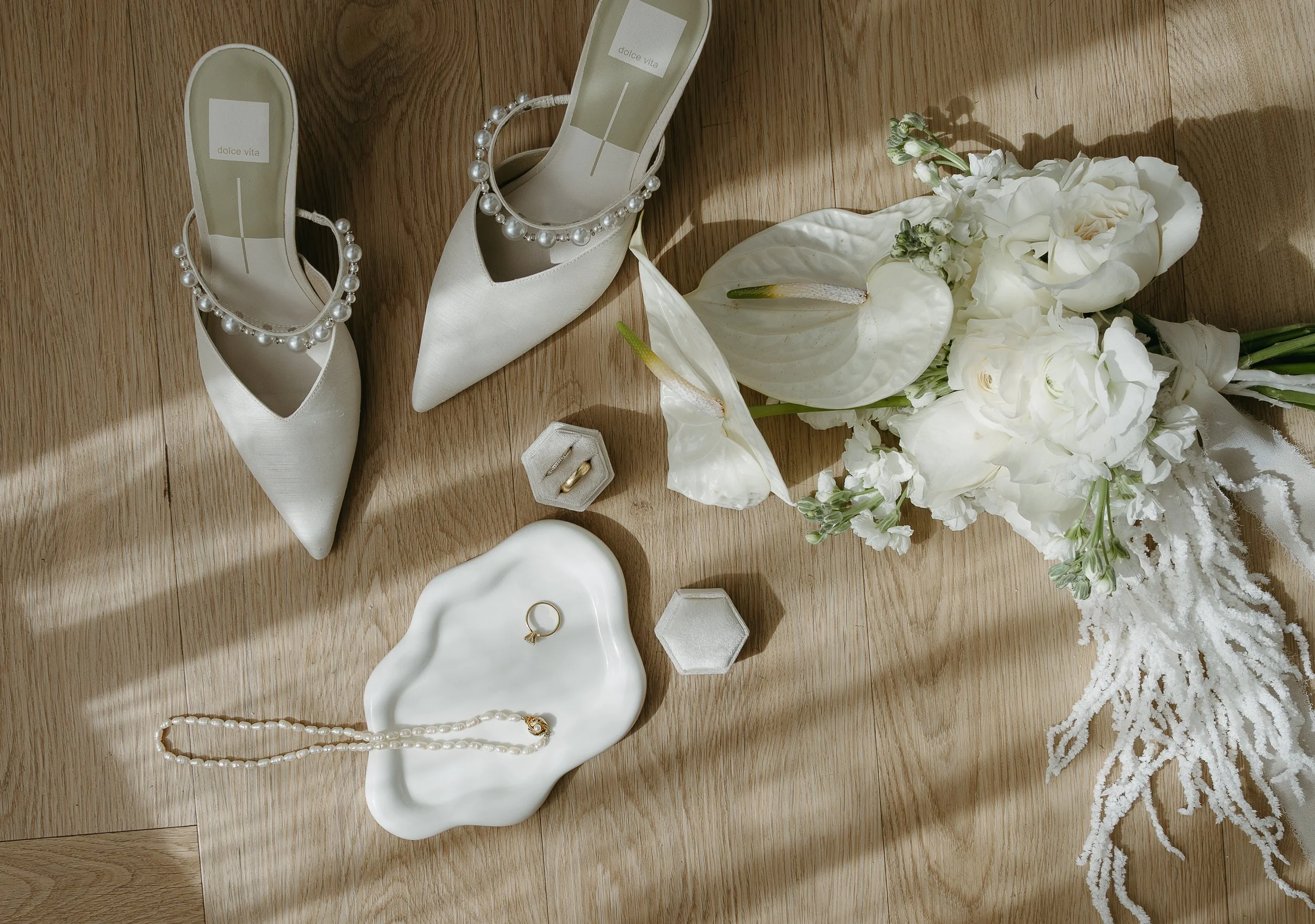 Wedding rings, a bouquet of flowers, and a brides wedding shoes or placed on a wooden table. Calgary Elopement/Wedding Editorial Session with KC Photography