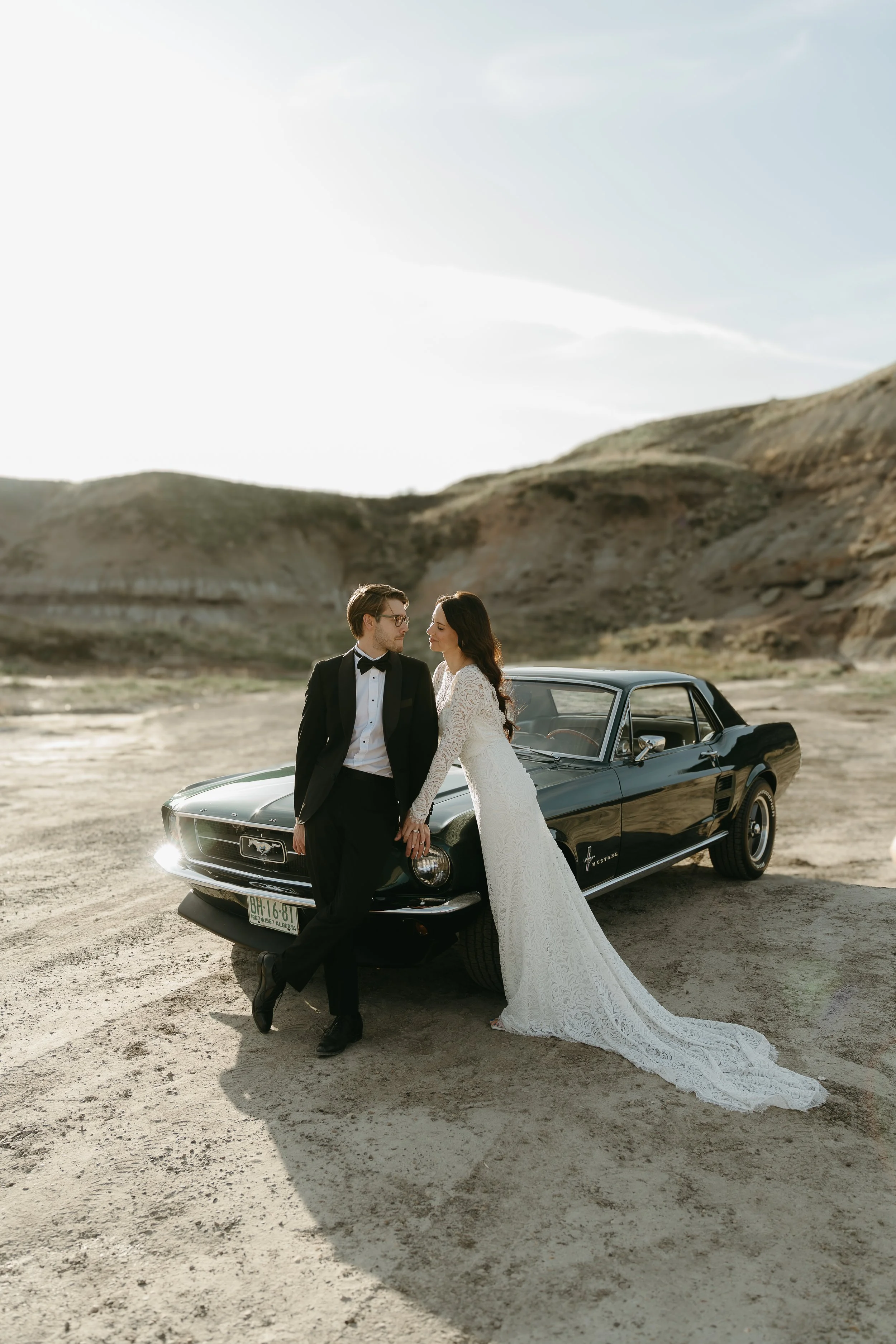badlands, drumheller alberta wedding photographer.   bride and groom stand in badlands of drumheller alberta with a vintage mustang