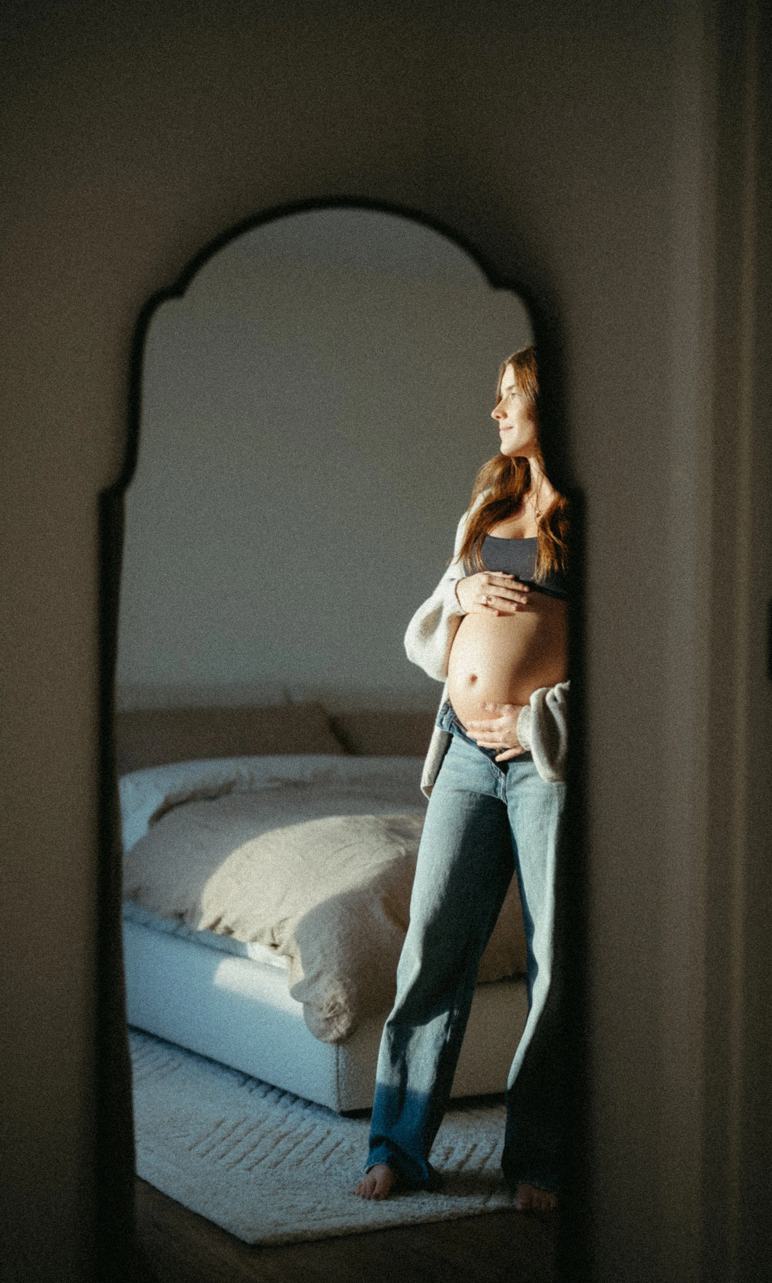 Calgary Alberta Maternity and Newborn Photographer.  Mom to be looking out the window, captured in the light of the day in a mirror reflection