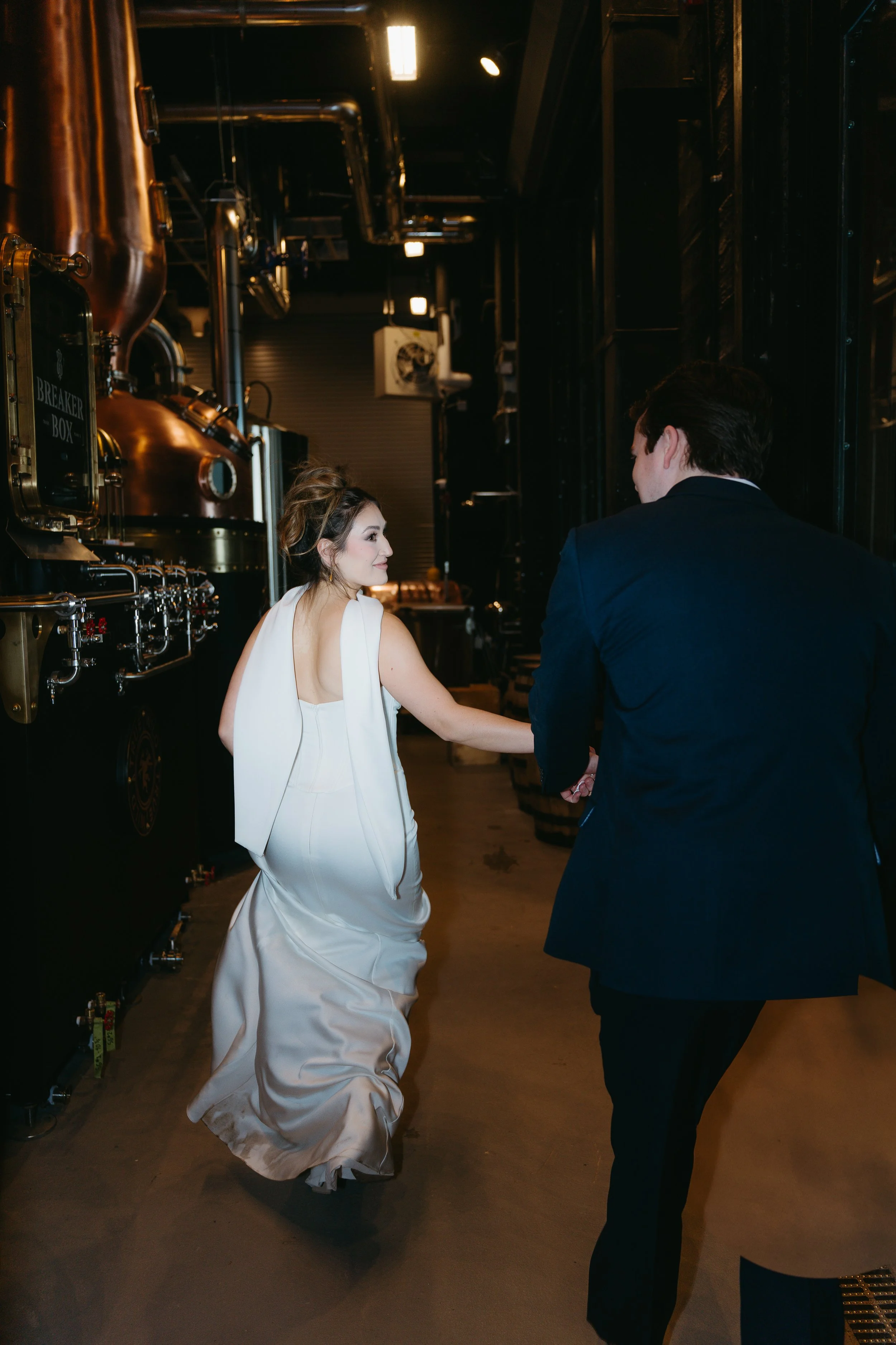 A bride and groom hold hands while running down a dimly lit industrial hallway. Calgary Elopement/Wedding Session with KC Photography