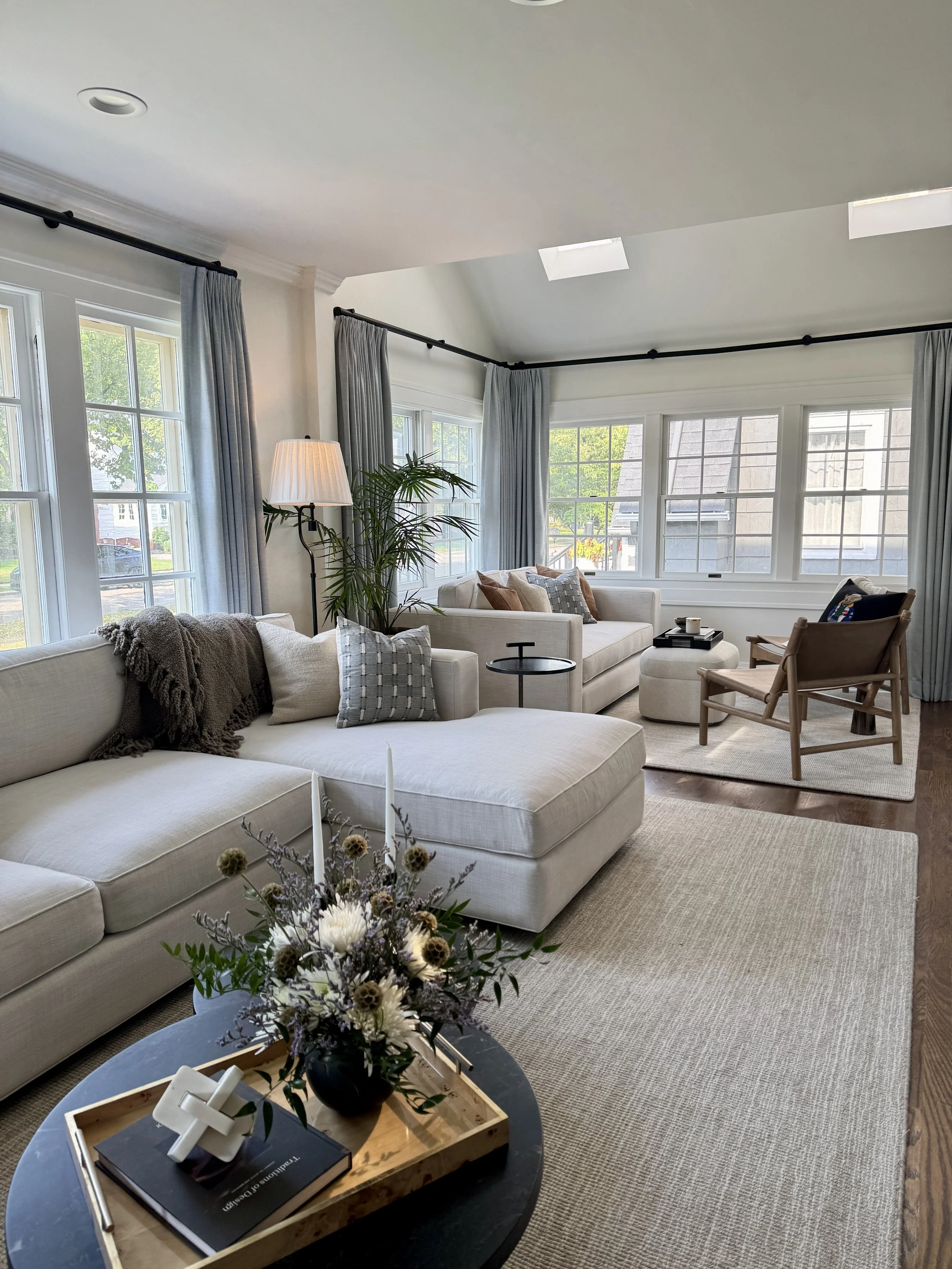 A refined entryway with decorative wall trim, a modern chandelier, curated artwork, and statement sconces. A blue velvet sofa on a soft beige rug completes the look.