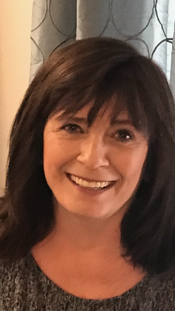 A smiling woman with shoulder-length dark brown hair in front of a patterned curtain.