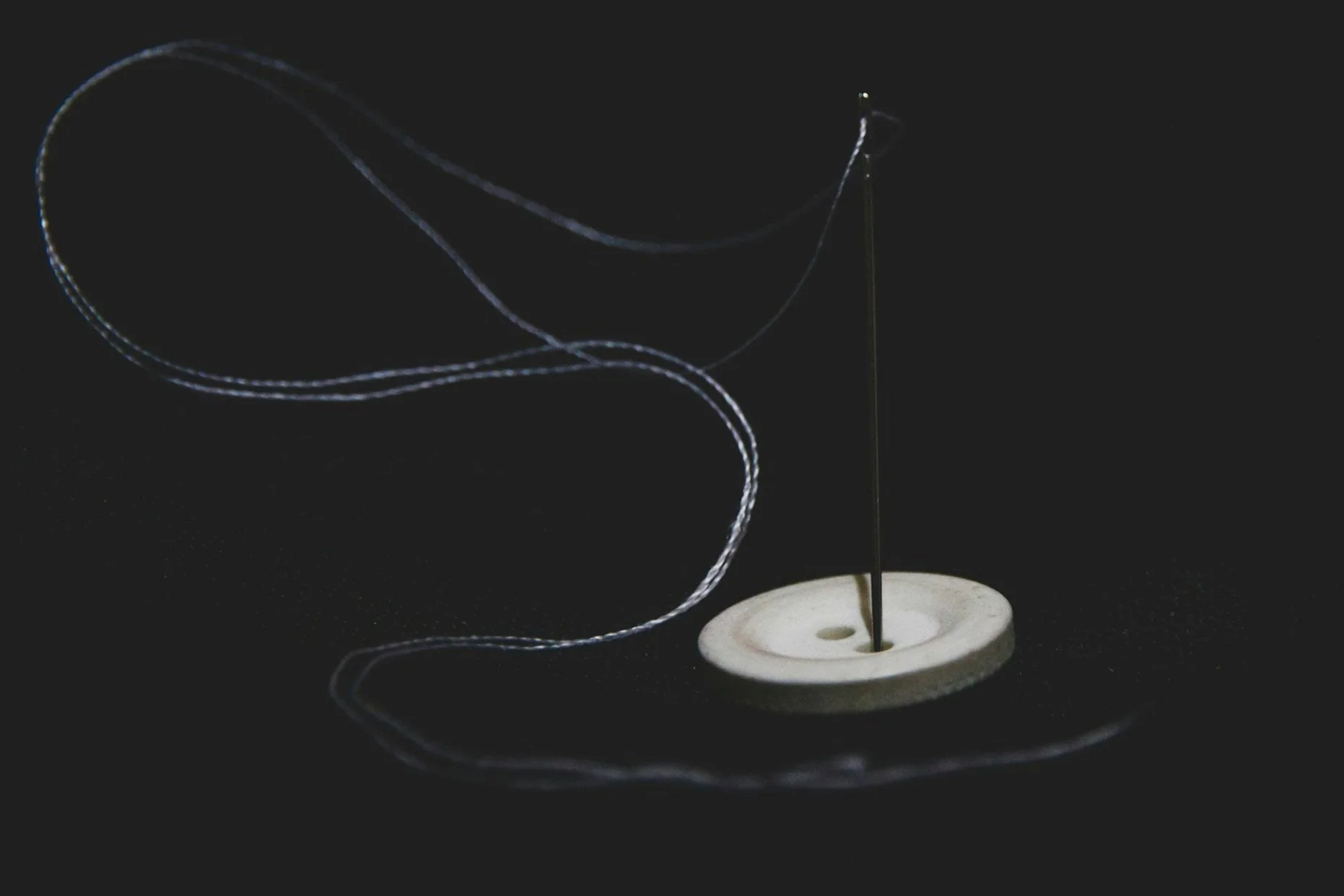 Close-up of a small magnetic or metal object on a white surface with a thin, upward-pointing needle and a thin wire or filament creating loops in the air against a dark background.