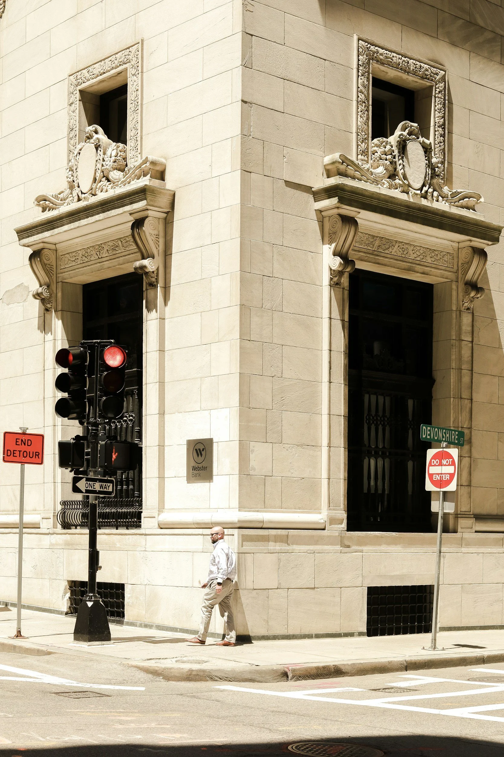 A man crossing the street at an intersection with traffic signals, street signs, and building architecture visible.