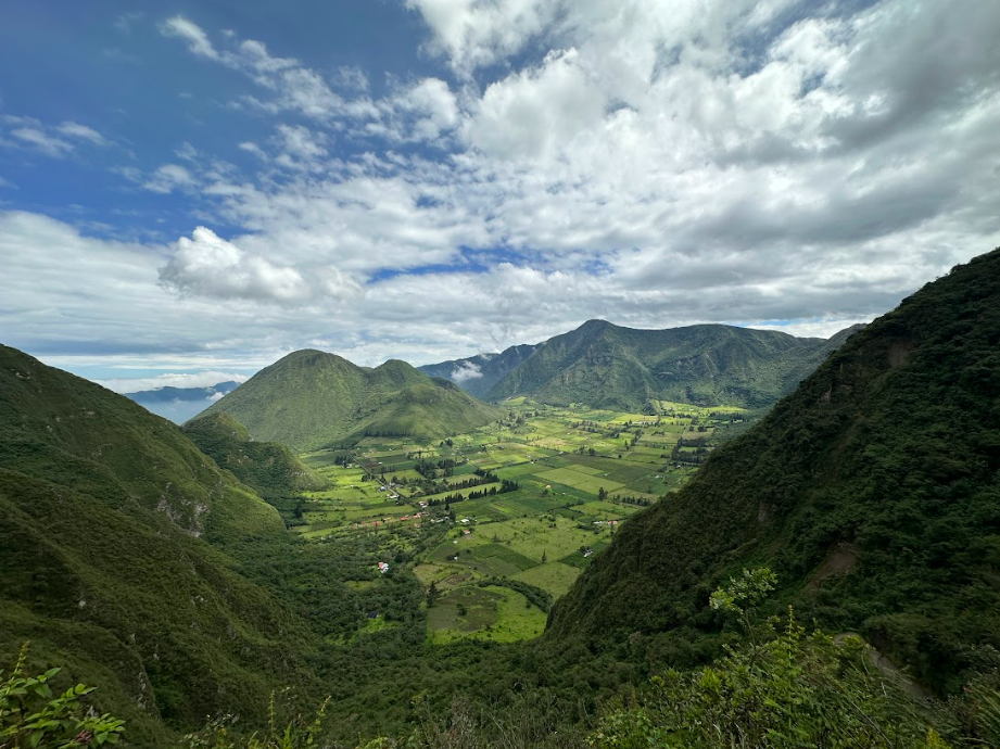 A lush green valley surrounded by tall mountains under a partly cloudy sky.
