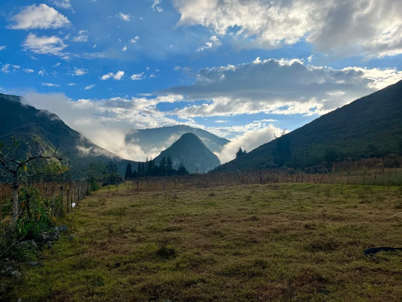 A scenic view of green rolling hills and mountains under a partly cloudy sky with patches of blue.
