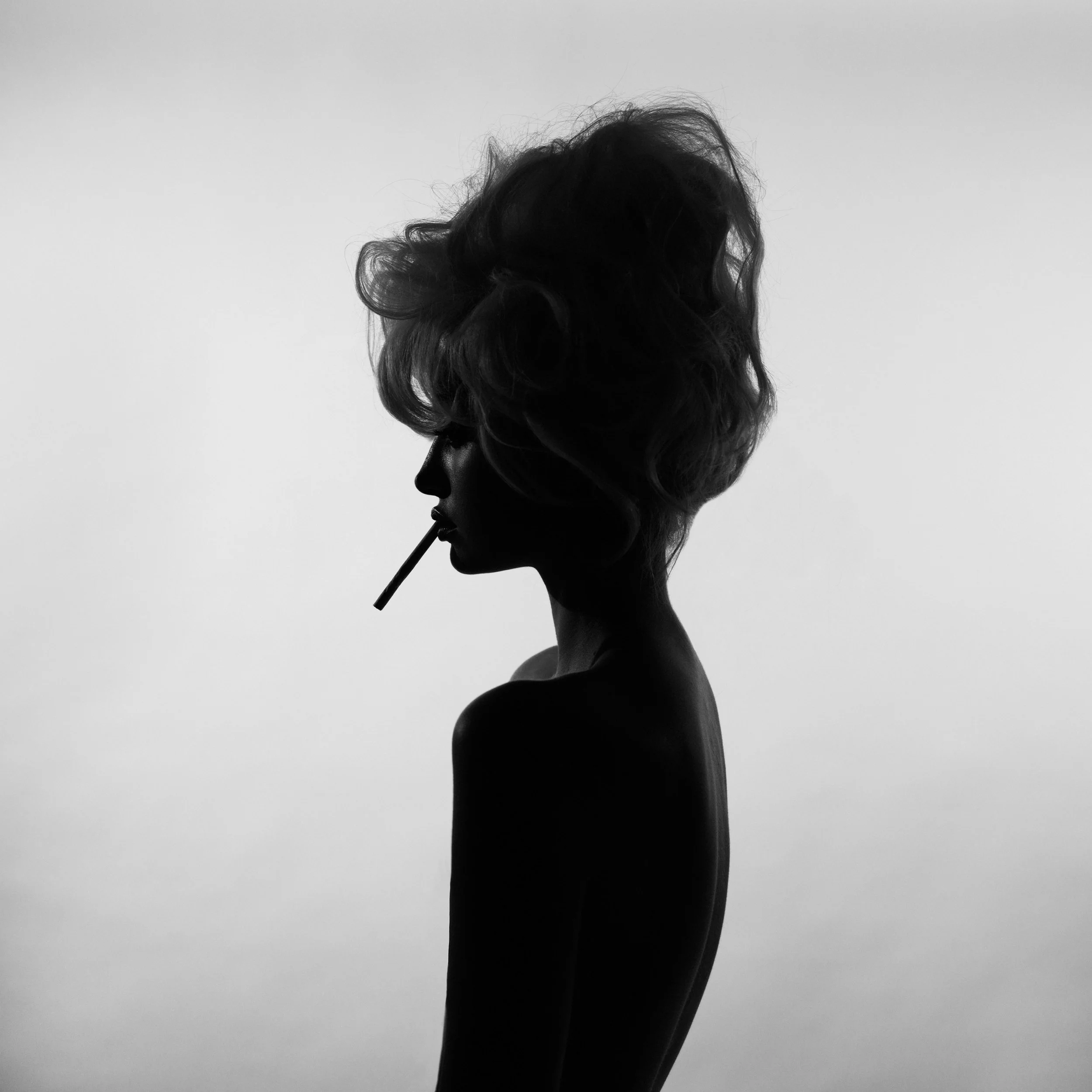 Silhouette of a woman with curly hair holding long-stemmed cigarette against a light gray background.