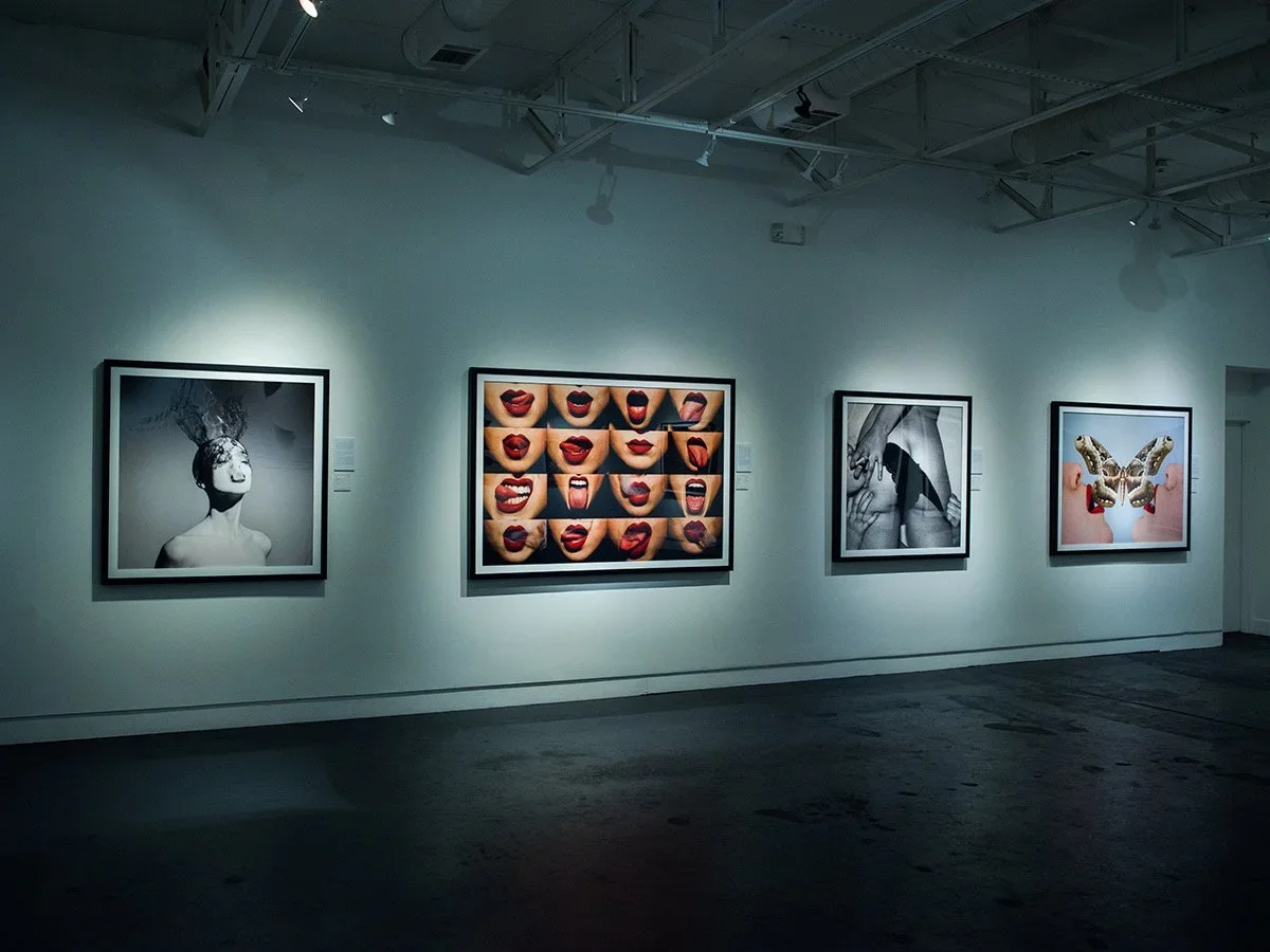 Gallery wall with four framed art pieces: first is a black and white photo of a woman with smoke coming out of her head, second features multiple close-up images of mouths with red lipstick, third shows a black and white photo of hands touching a belly, fourth displays a butterfly with lips and hands in the background.